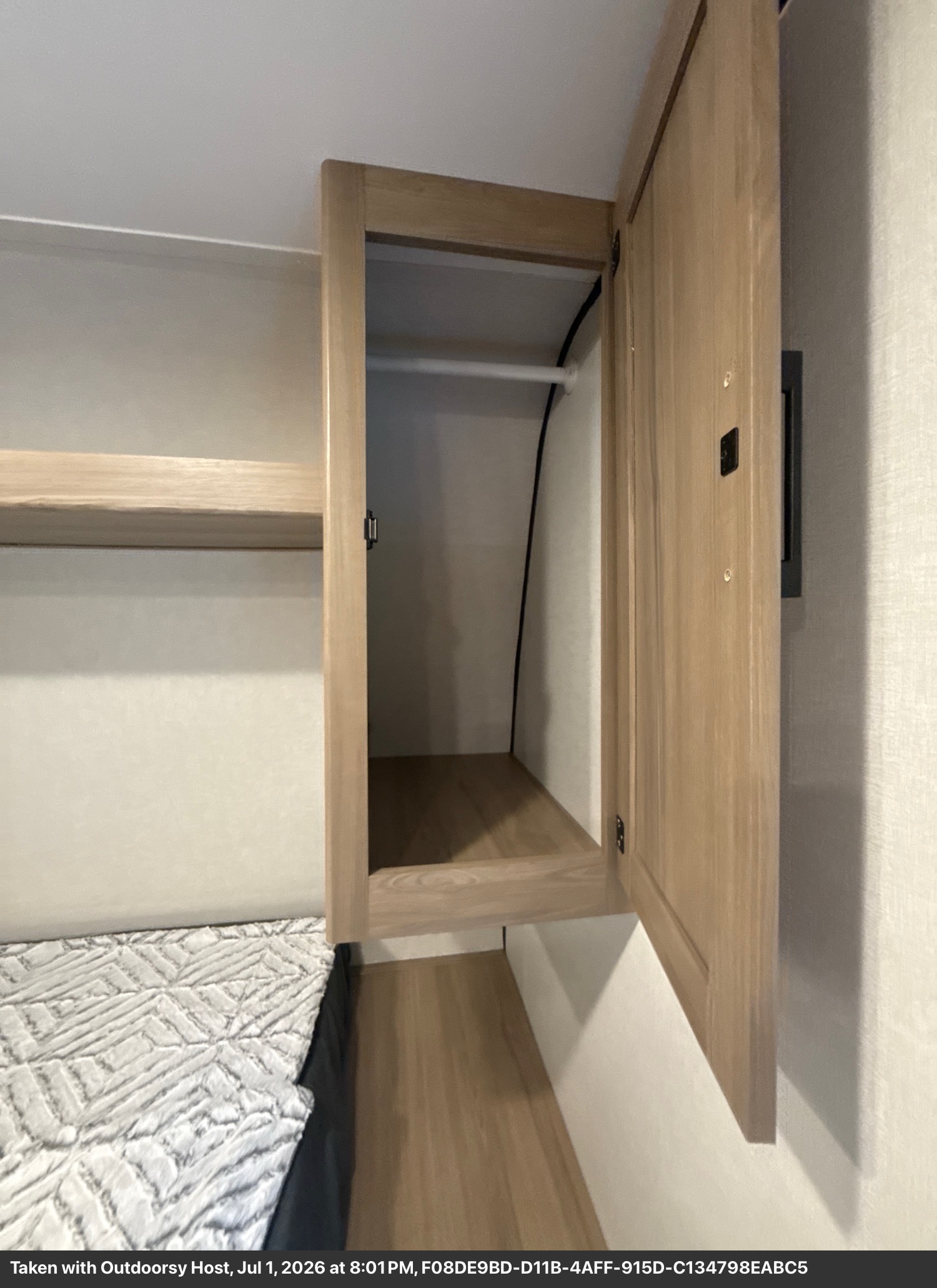 Compact RV rental bedroom featuring an open wardrobe with a hanging rod, bottom shelf, and a bed with textured bedding.. Keystone Coleman 17B 2026