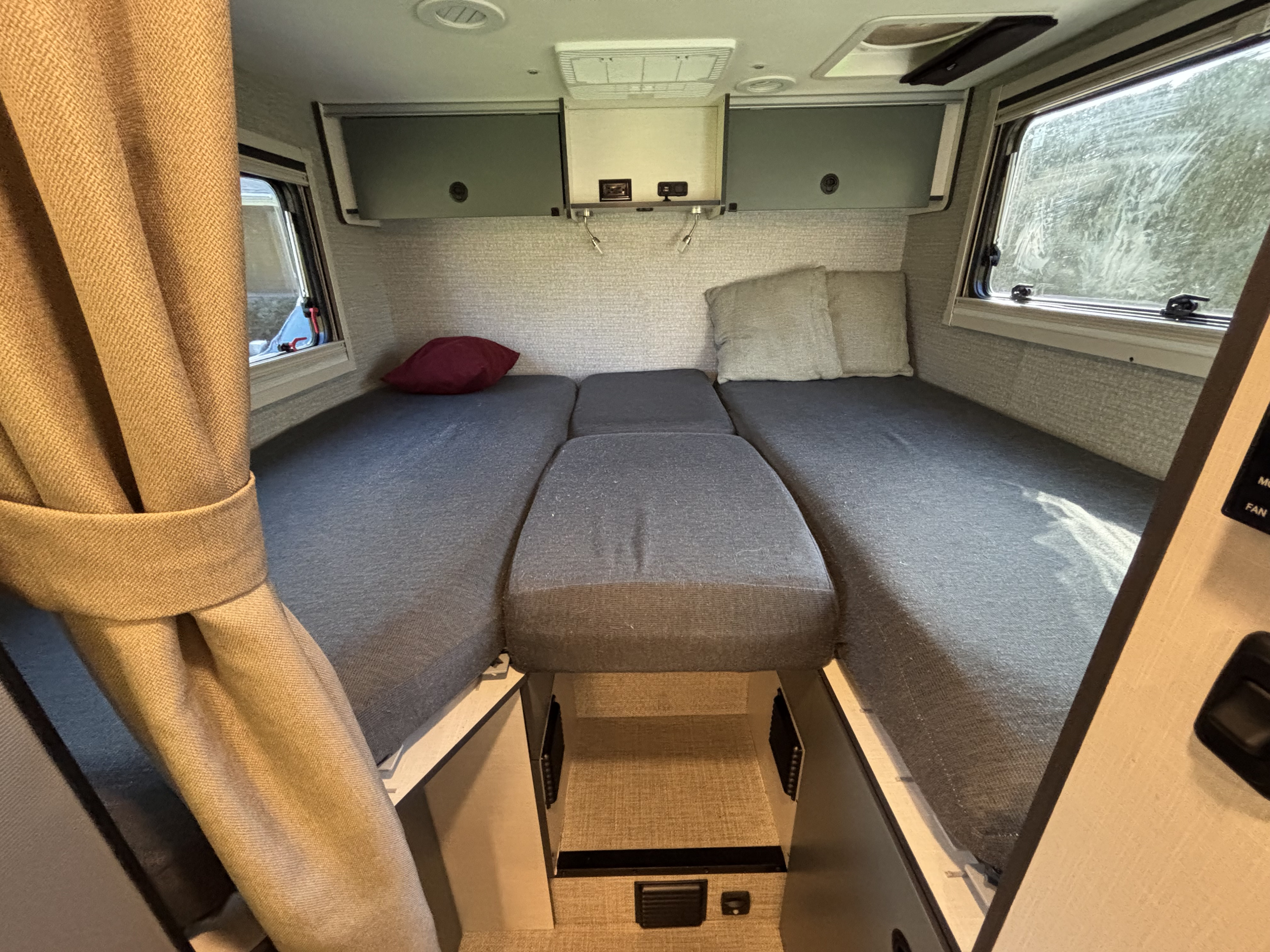 RV rental interior: twin beds with a convertible middle cushion, overhead storage, and window views.. Winnebago Ekko 2023
