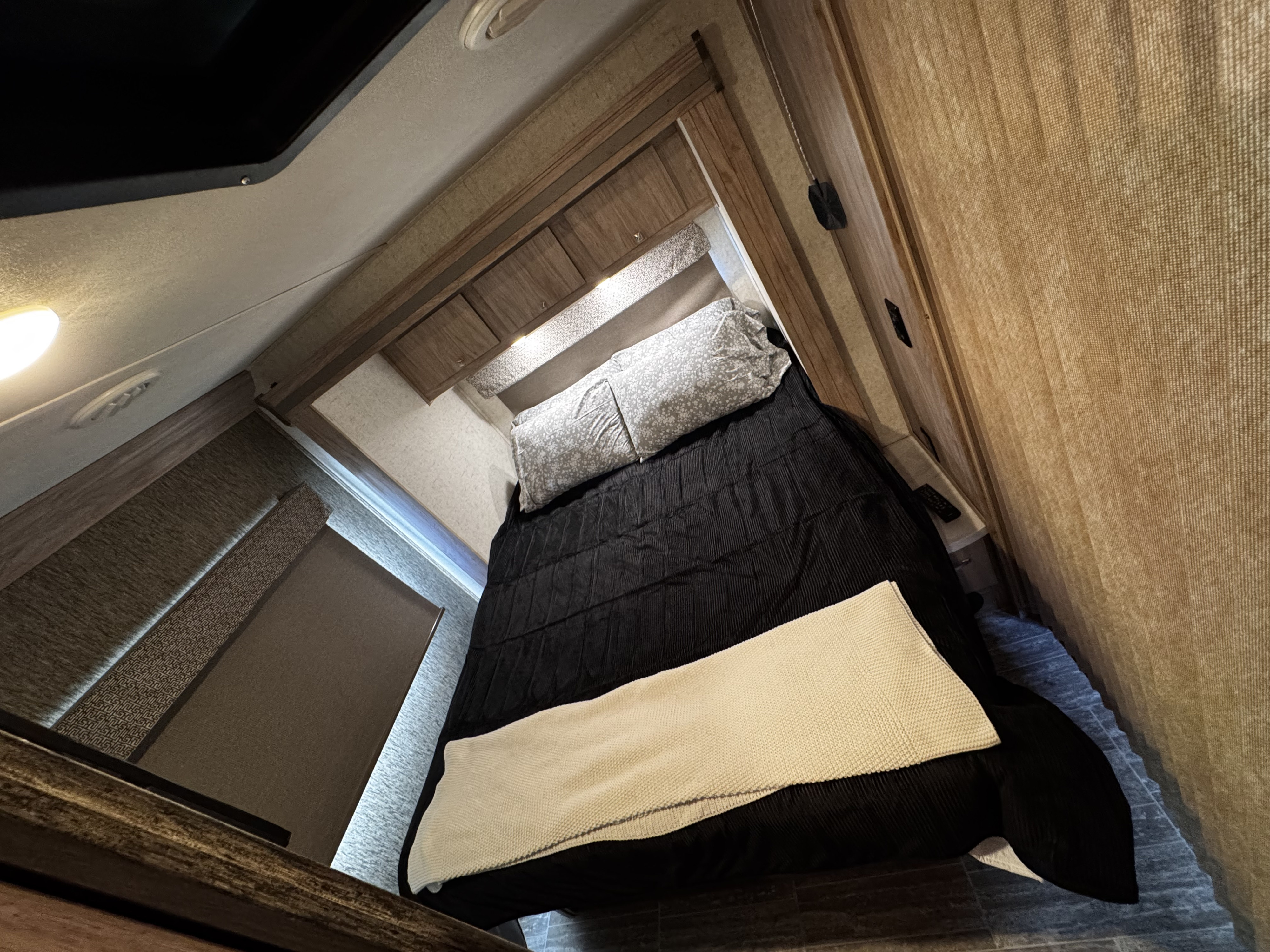 Cozy and compact RV rental bedroom with a bed, black bedding, patterned pillows, and convenient overhead storage cabinets.. Forest River Sunseeker LE 2018