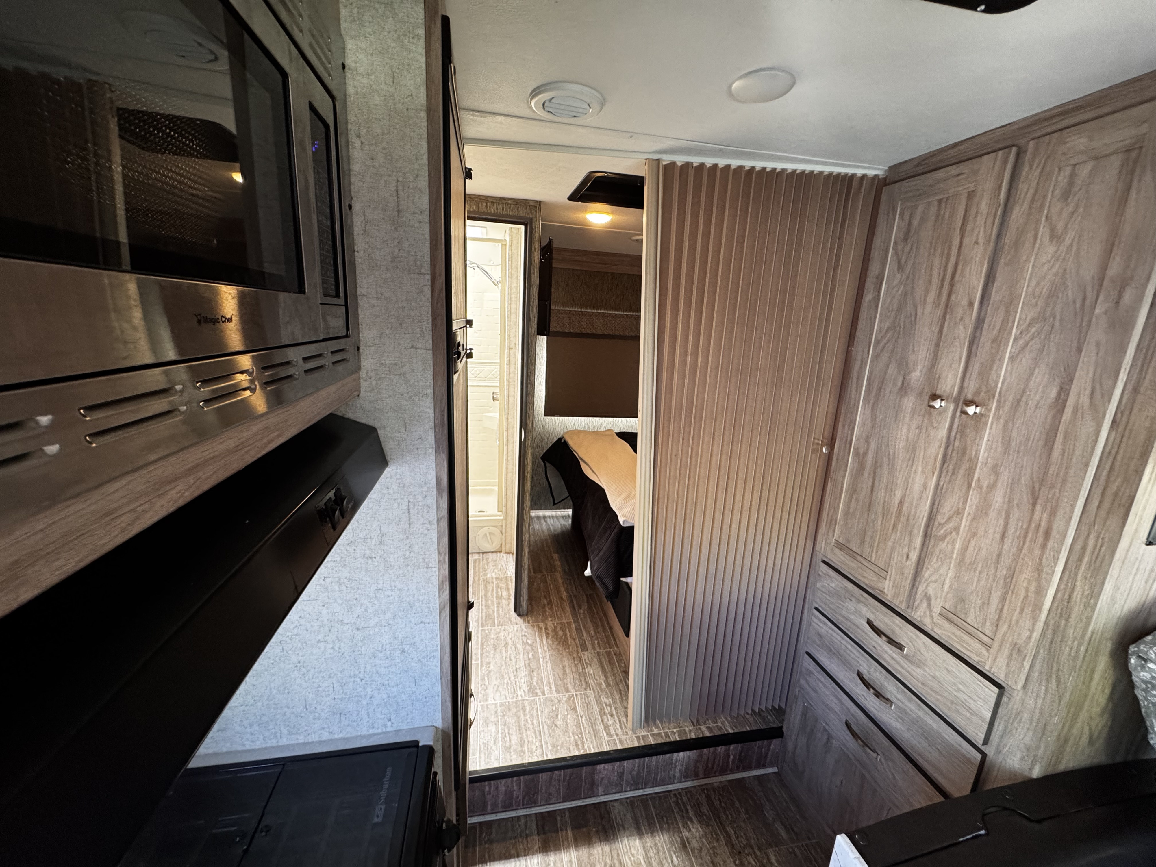 Explore this rv rental interior: compact kitchen with microwave, hallway leading to bathroom and bedroom, and wood cabinets.. Forest River Sunseeker LE 2018