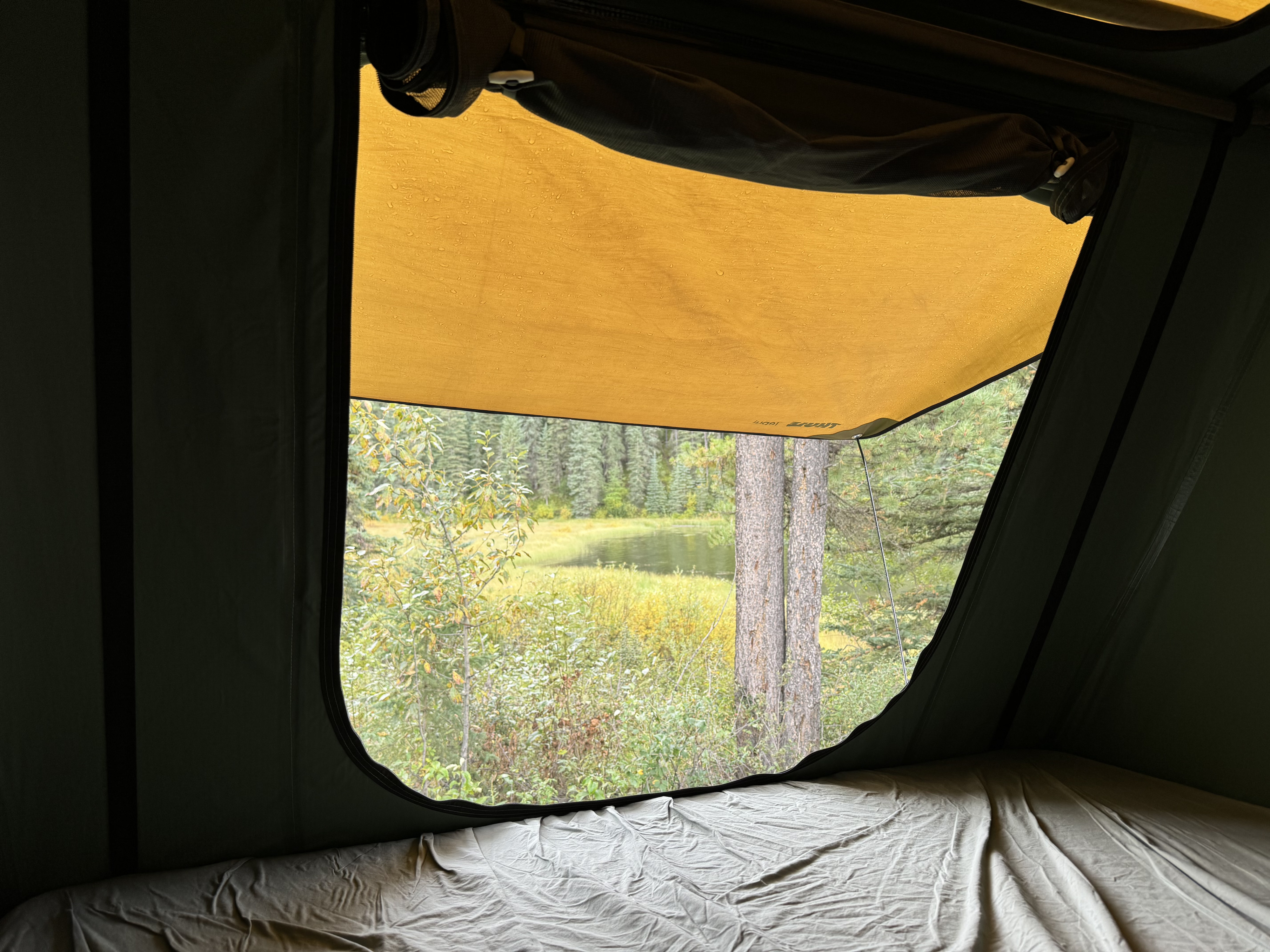 Cozy view from an RV rental rooftop tent, overlooking a tranquil lake and forest on a damp day.. Volvo XC60 2022