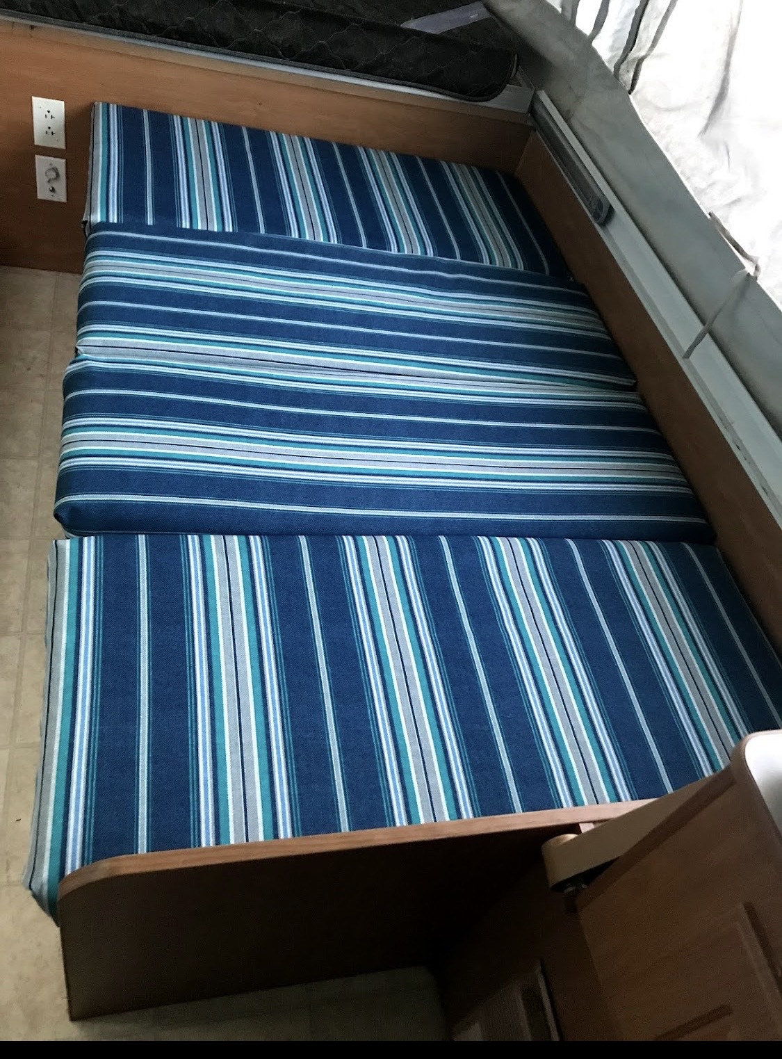 This RV rental interior features striped blue & white cushions on wooden bases, forming a comfy sleeping/seating area.. Coleman Santa Fe 2003