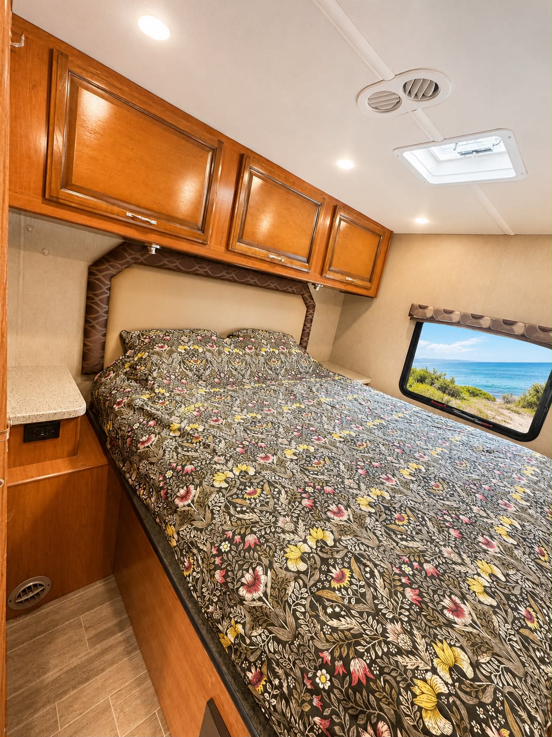 RV rental bedroom with a large bed, colorful floral duvet, wood cabinets, and an ocean view out the window.. Jamboree Jamboree Motorhome 2018
