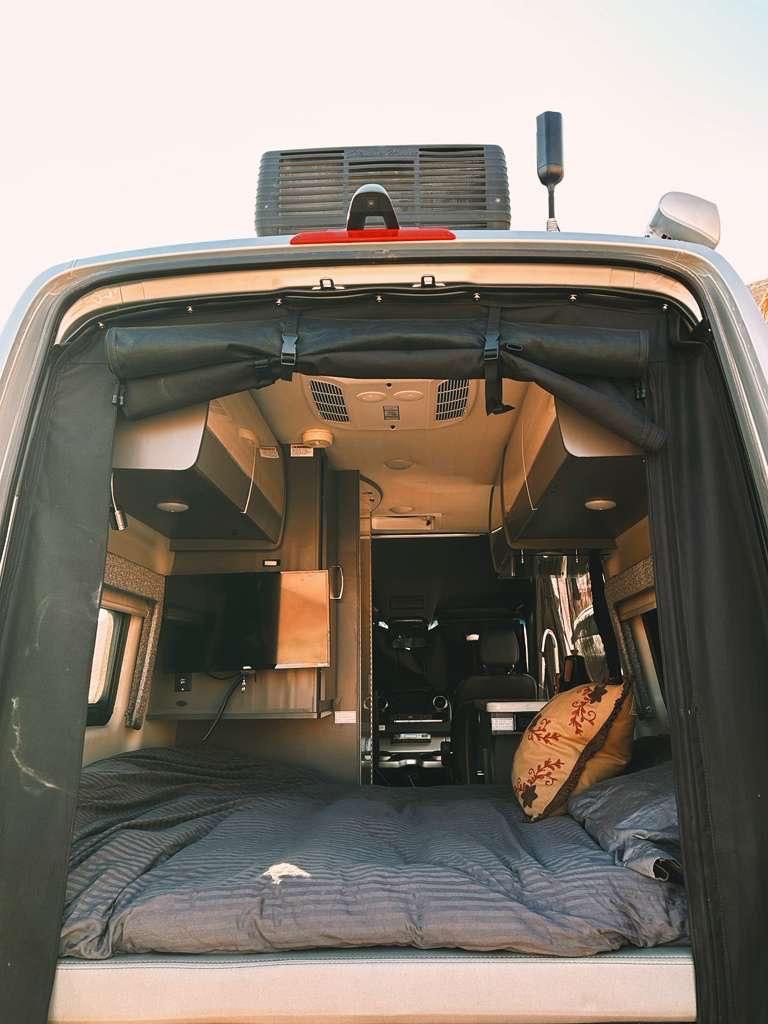 Cozy RV rental interior, viewed from open back doors, features a comfortable bed, mounted TV, and modern amenities for mobile living.. Thor Tranquility 2023