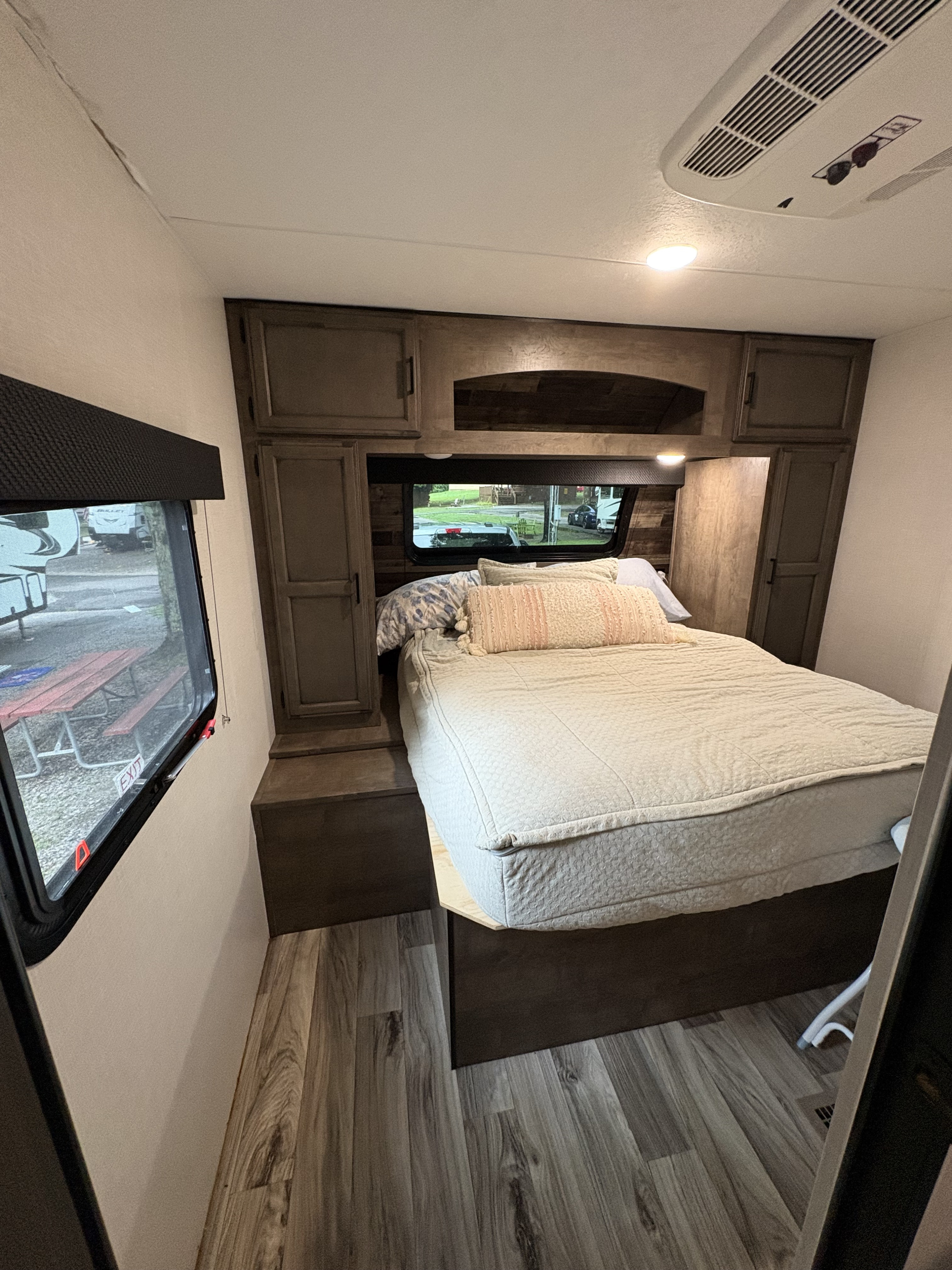 Cozy RV rental bedroom featuring a comfy bed, wooden cabinets, window views, and a ceiling AC unit.. Venture Venture Trailer 2023