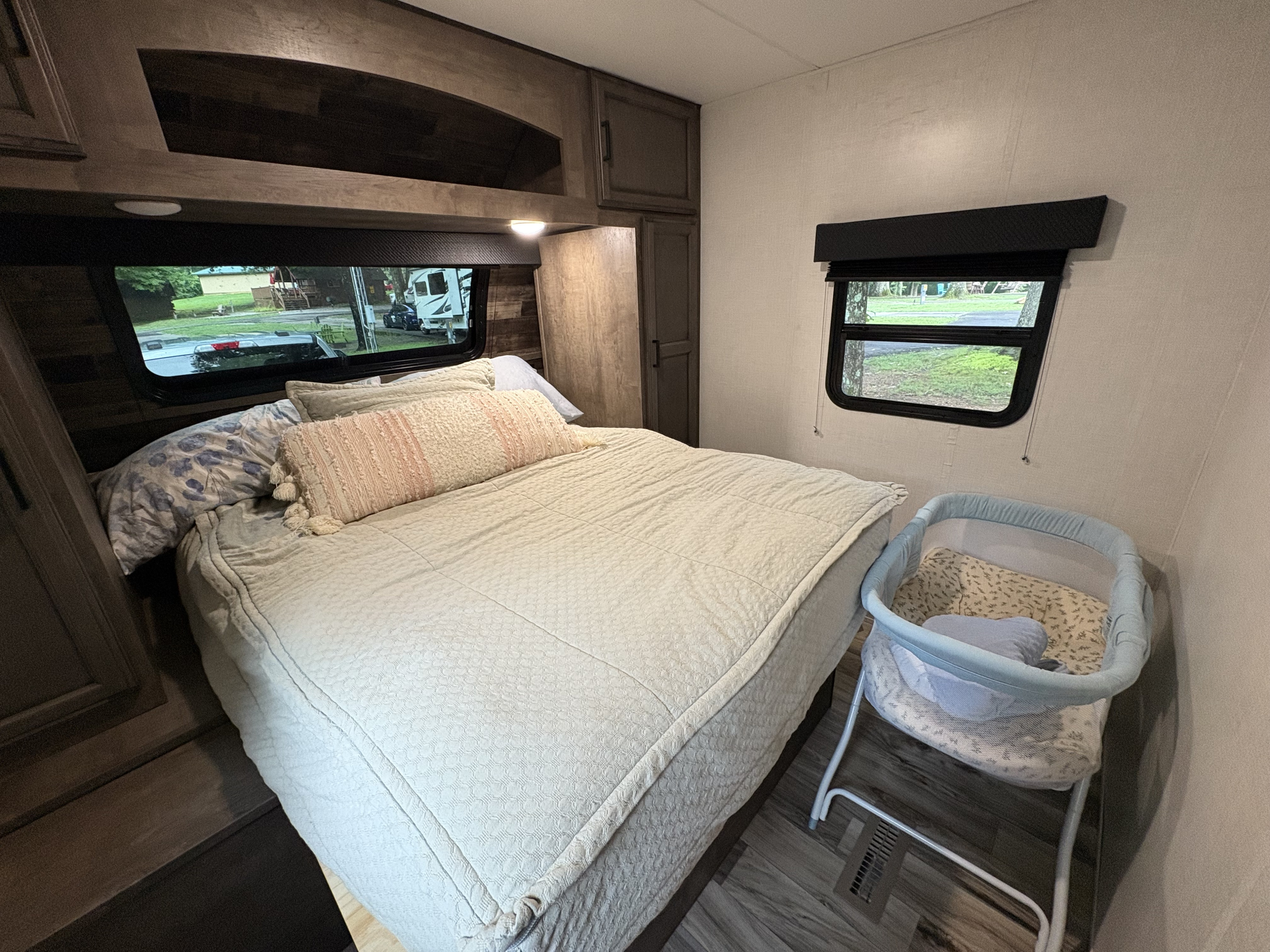 Cozy RV rental bedroom featuring a large bed, overhead storage, and a baby bassinet on the right, great for family stays.. Venture Venture Trailer 2023