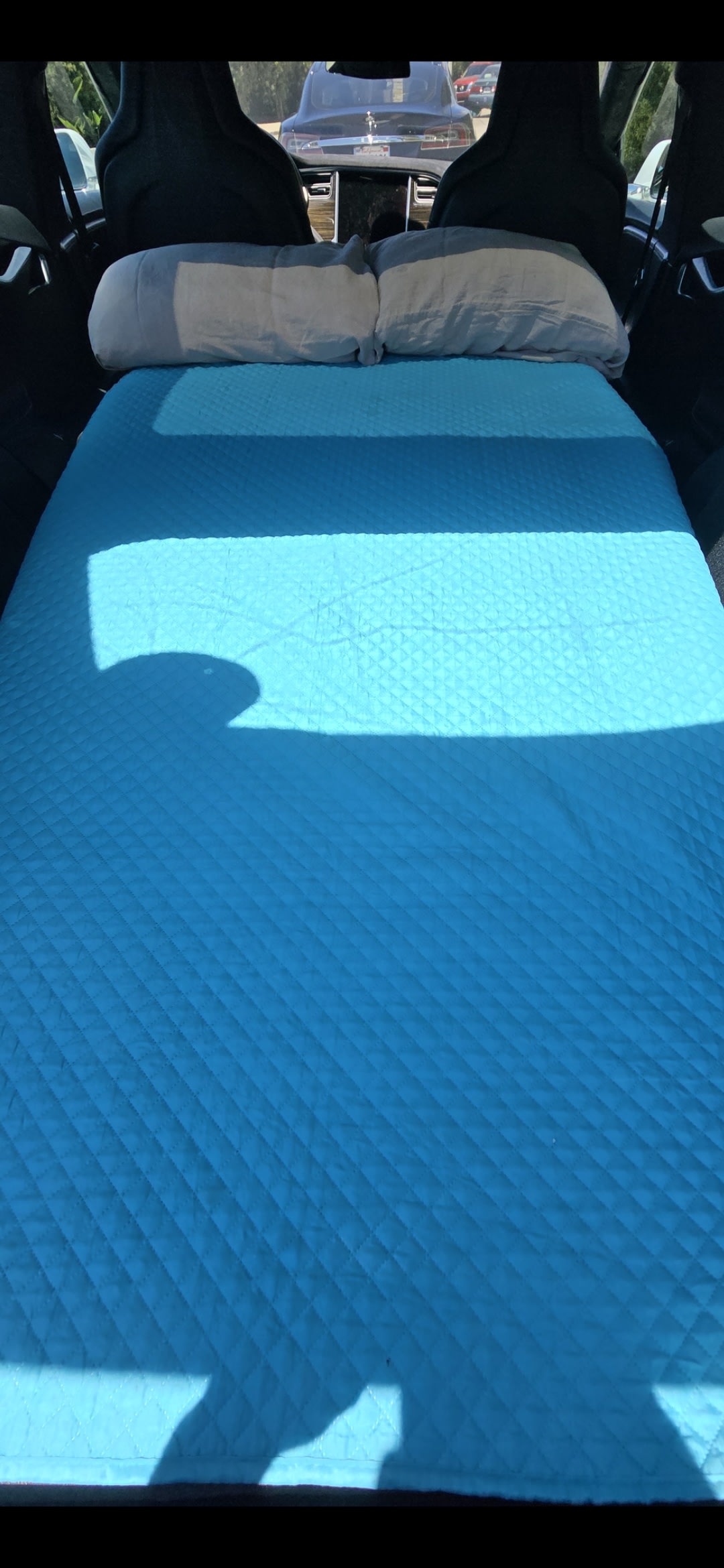 Blue quilted mattress and pillows make a cozy vehicle bed for car camping, a flexible alternative to an RV rental for travel.. Tesla S 2015