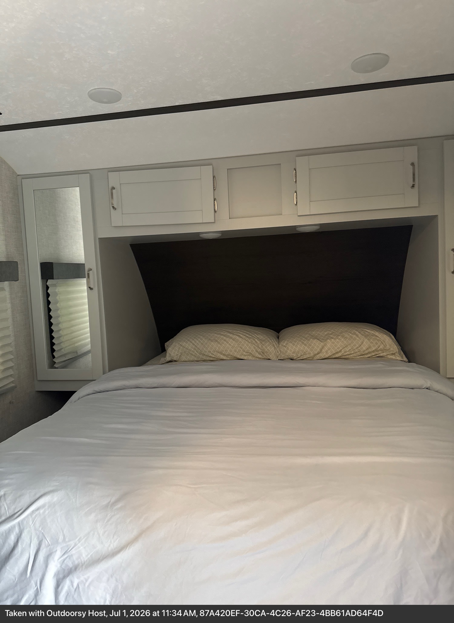 This cozy RV rental bedroom features a neatly made bed, overhead cabinets, a dark headboard, and a mirrored wardrobe.. Keystone RV Bullet Ultra Lite 2020