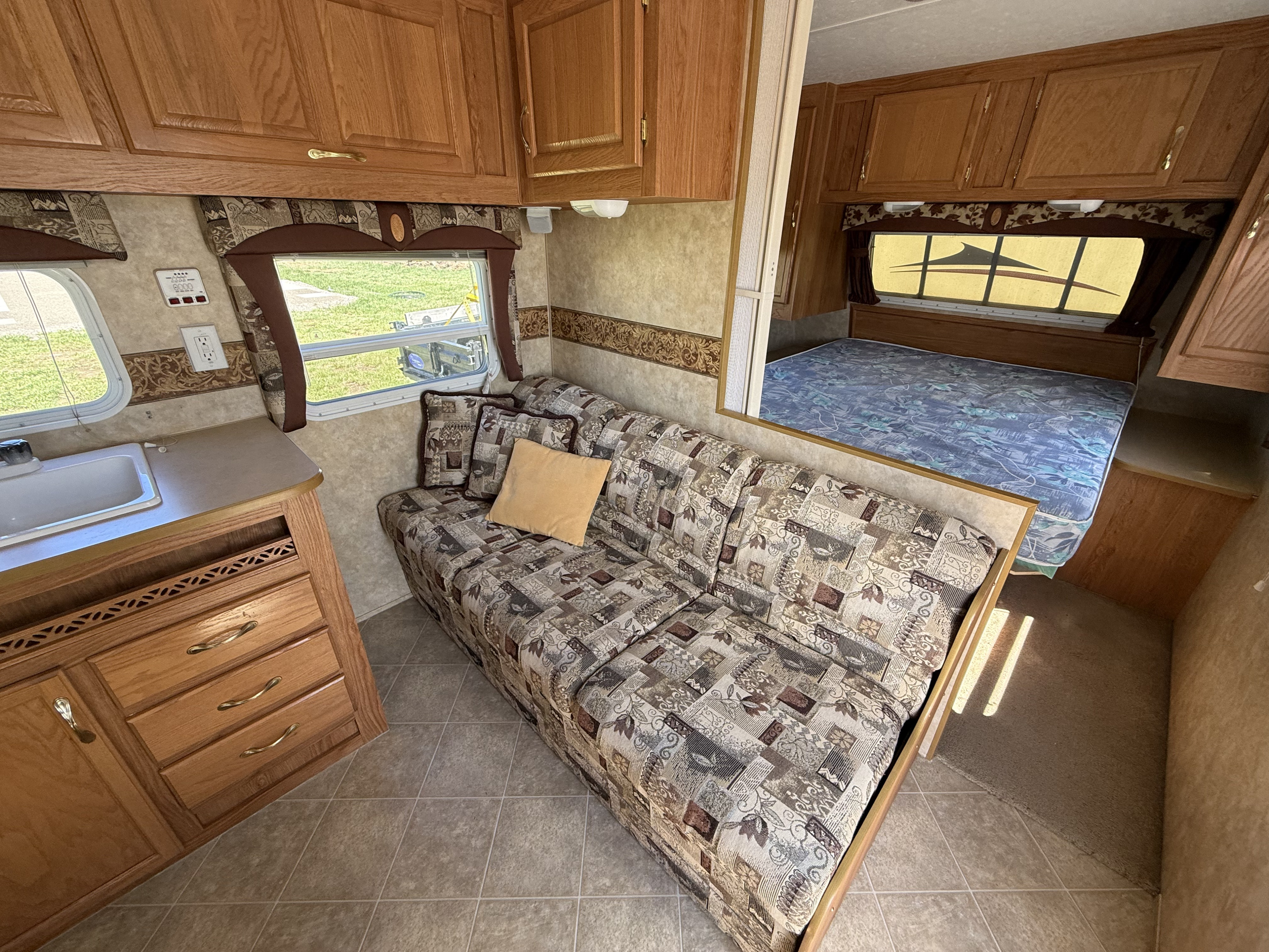 RV rental living space: kitchen sink, comfy patterned sofa, bed, wood cabinets, and windows offering natural light.. Jayco Jay Flight 2006