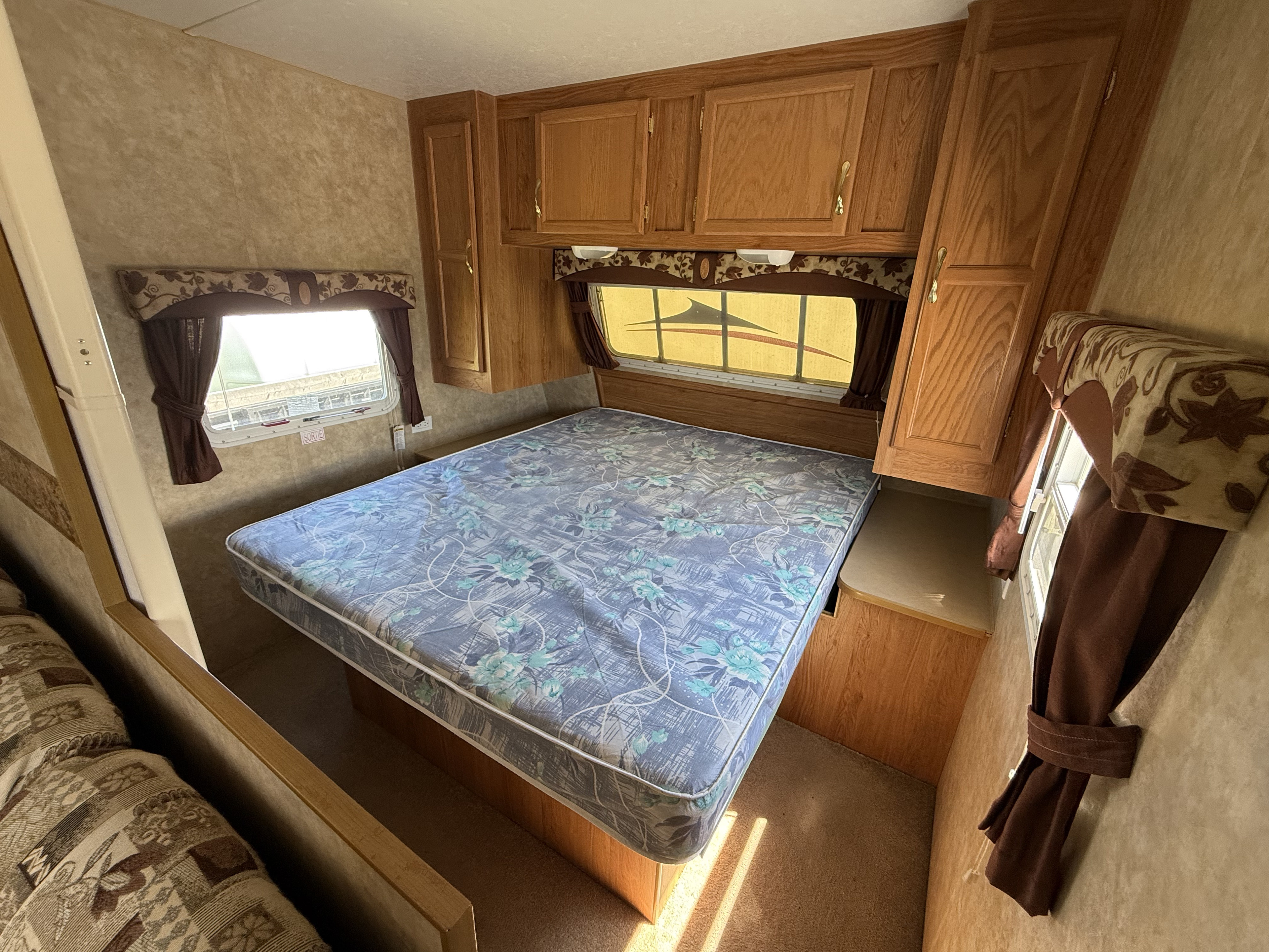 Spacious RV rental bedroom featuring a comfy floral mattress, light wood overhead cabinets, and large windows with curtains.. Jayco Jay Flight 2006