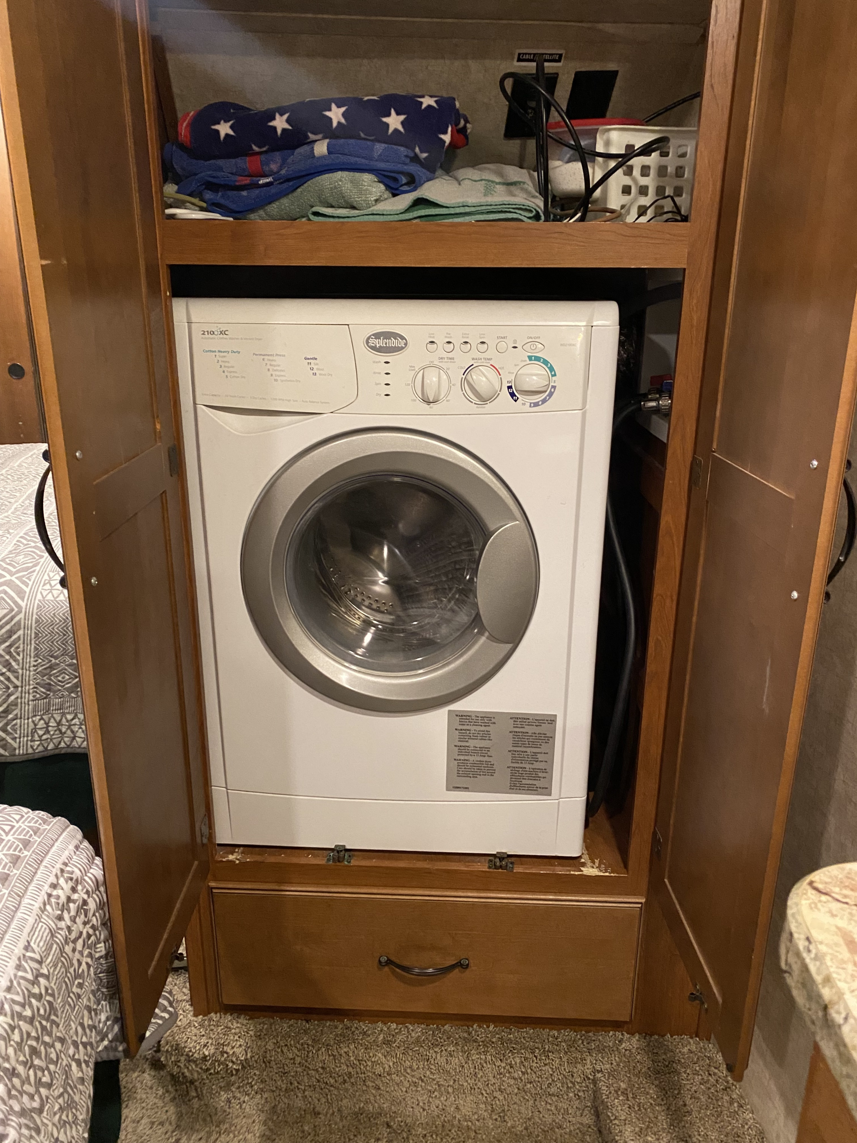 A white Splendide compact washer/dryer combo integrated into a wooden cabinet in an RV, perfect for rv rental trips.. Keystone RV Montana High Country 2013