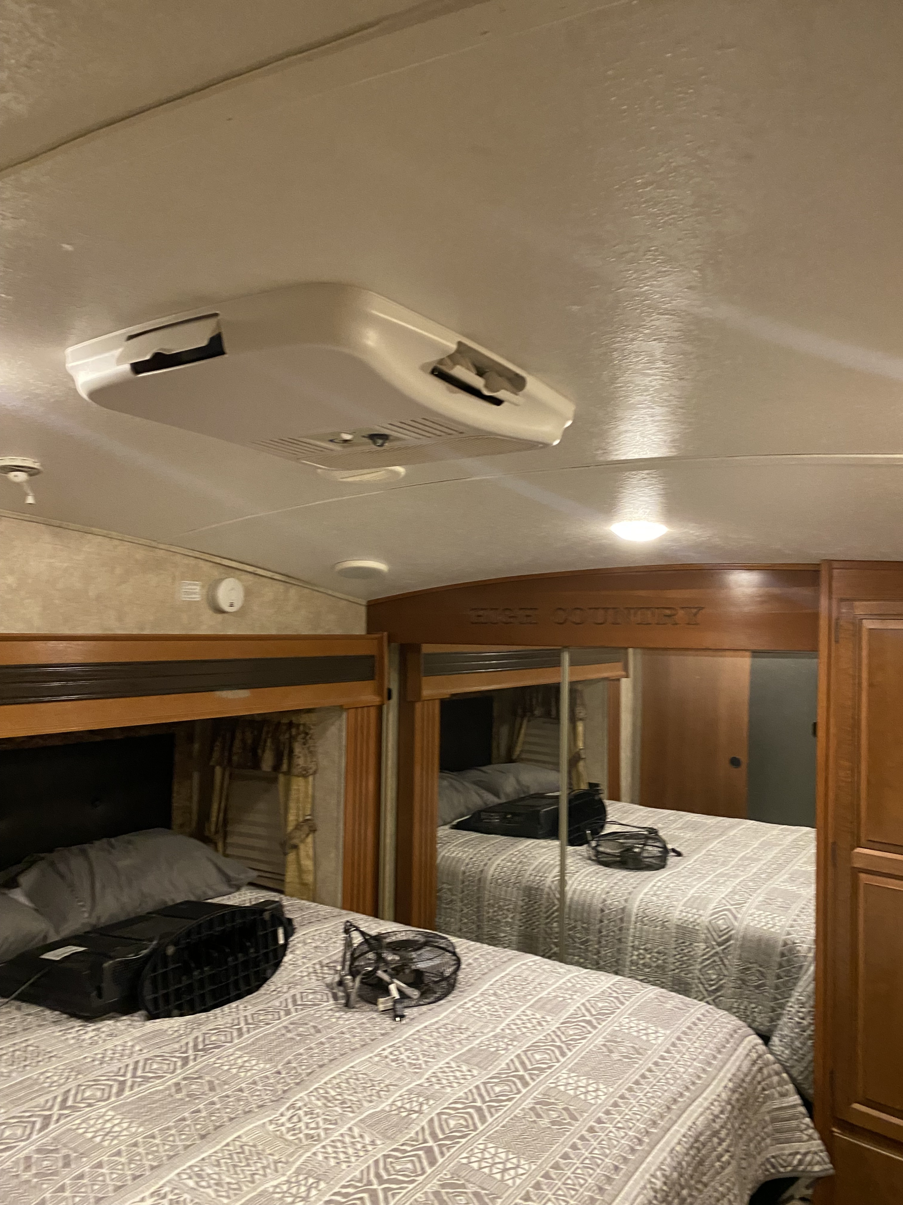 RV rental bedroom: a bed with patterned quilt, overhead AC unit, and mirrored closet. Ready for comfortable travel.. Keystone RV Montana High Country 2013