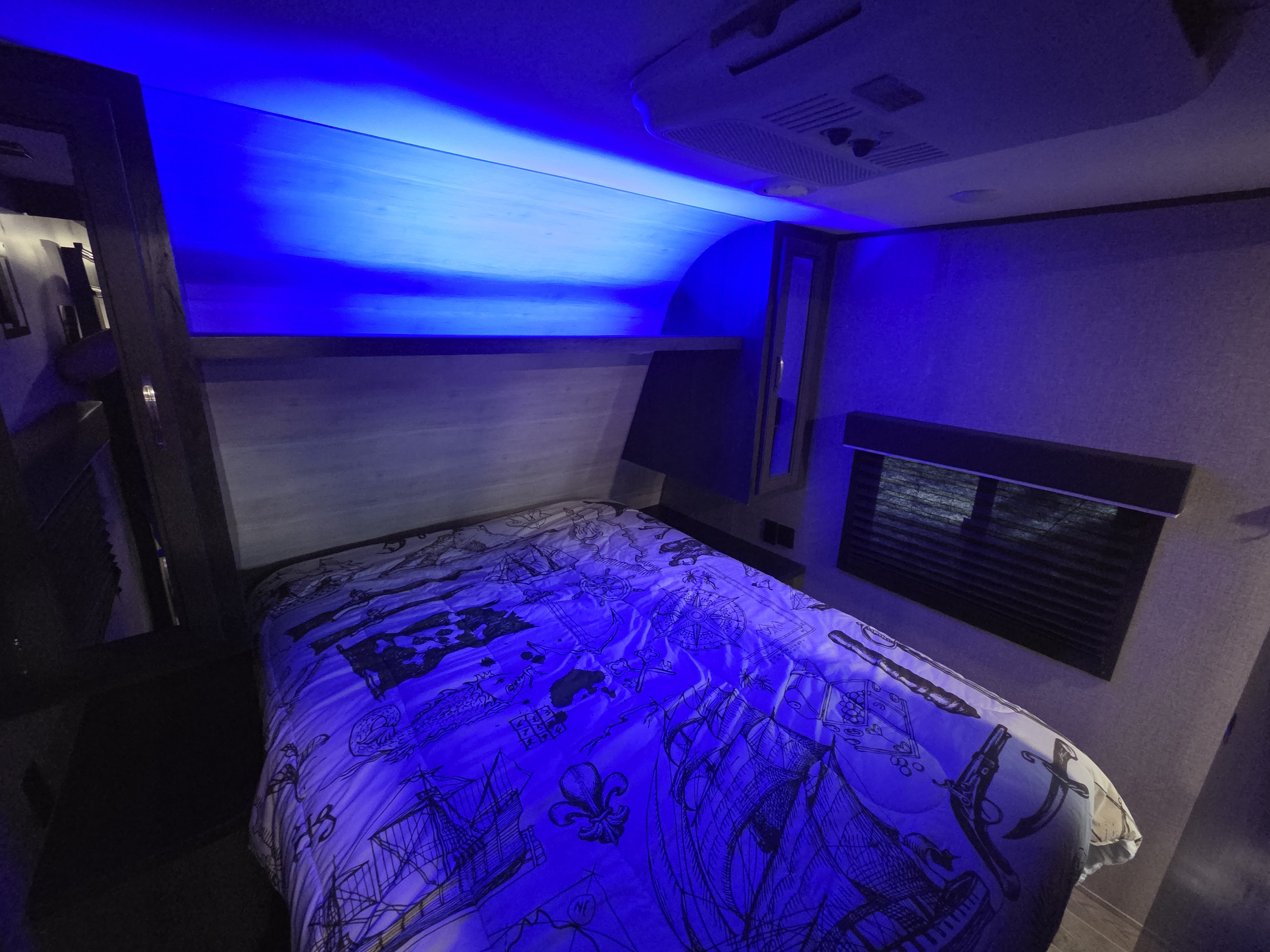 Cozy blue-lit RV rental bedroom. Features nautical bedding and overhead AC for comfortable travel adventures.. Jayco Jay Flight SLX 2021