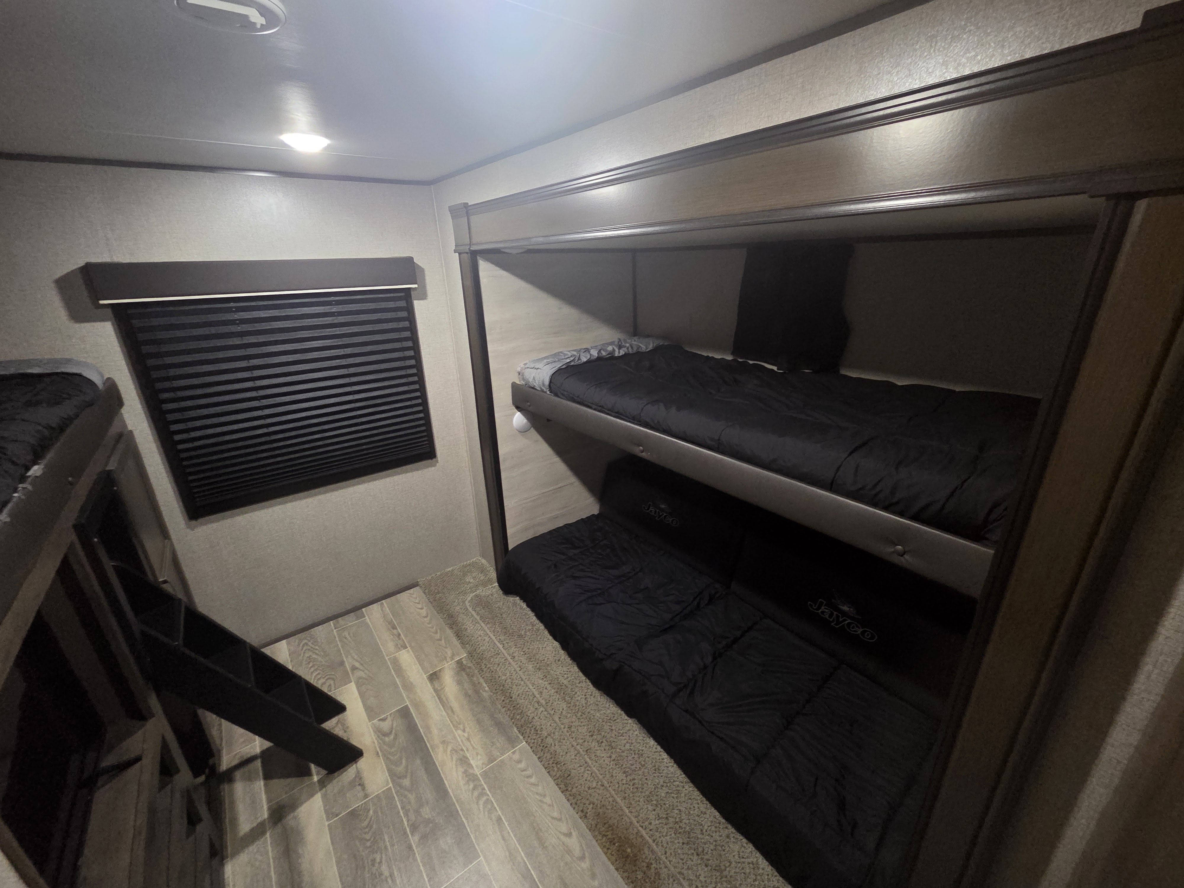 Bunk beds in an RV rental, featuring dark bedding, a window blind, and mixed wood-look and carpet flooring.. Jayco Jay Flight SLX 2021
