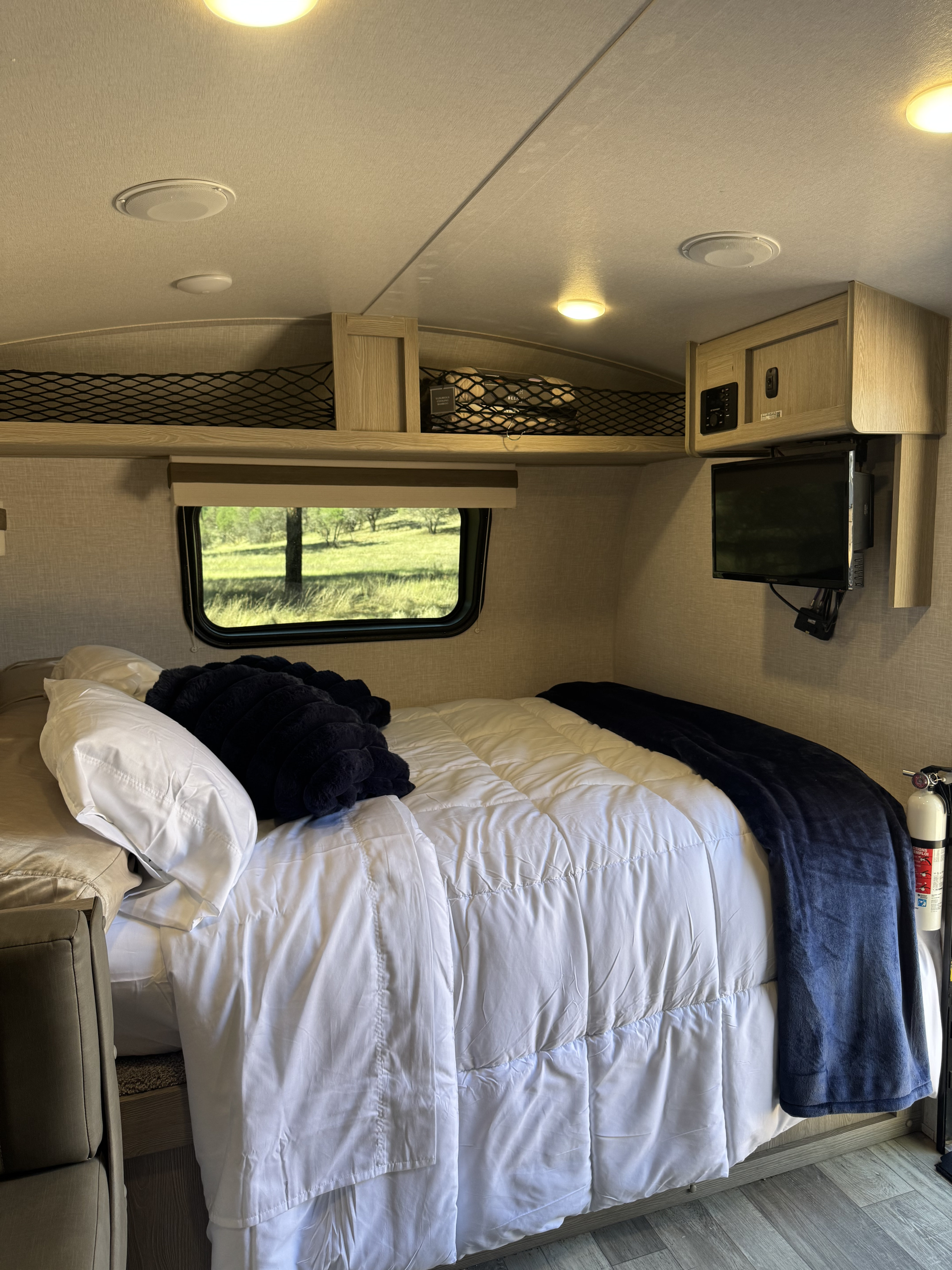 Inside a cozy rv rental bedroom: bed with blue blanket, scenic window, overhead storage, TV, and fire extinguisher.. Forest River Rockwood Geo Pro 2022
