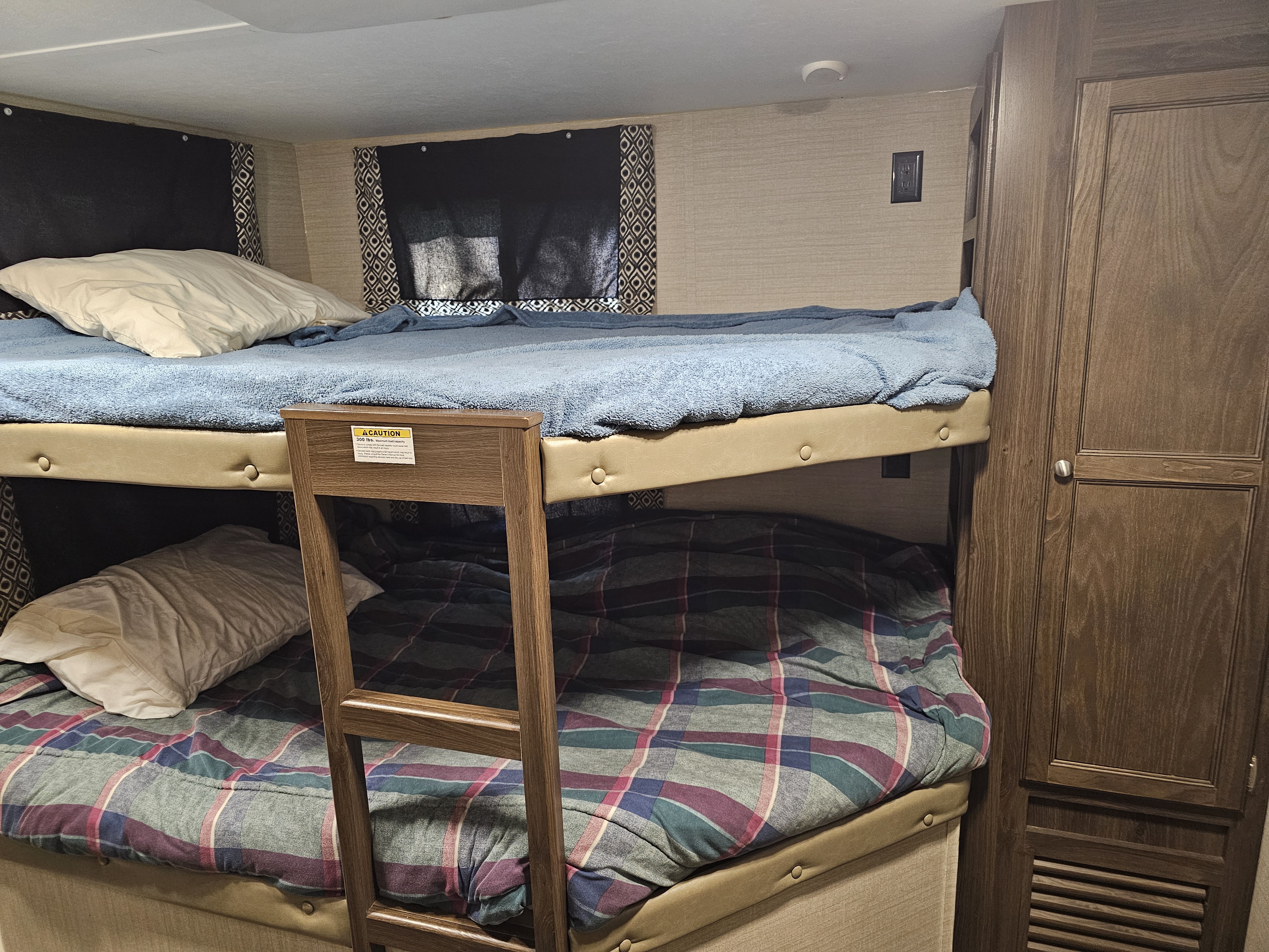 RV rental interior: cozy bunk beds with a ladder, pillows, blue and plaid blankets, and a storage cabinet.. Keystone RV Bullet Ultra Lite 2018