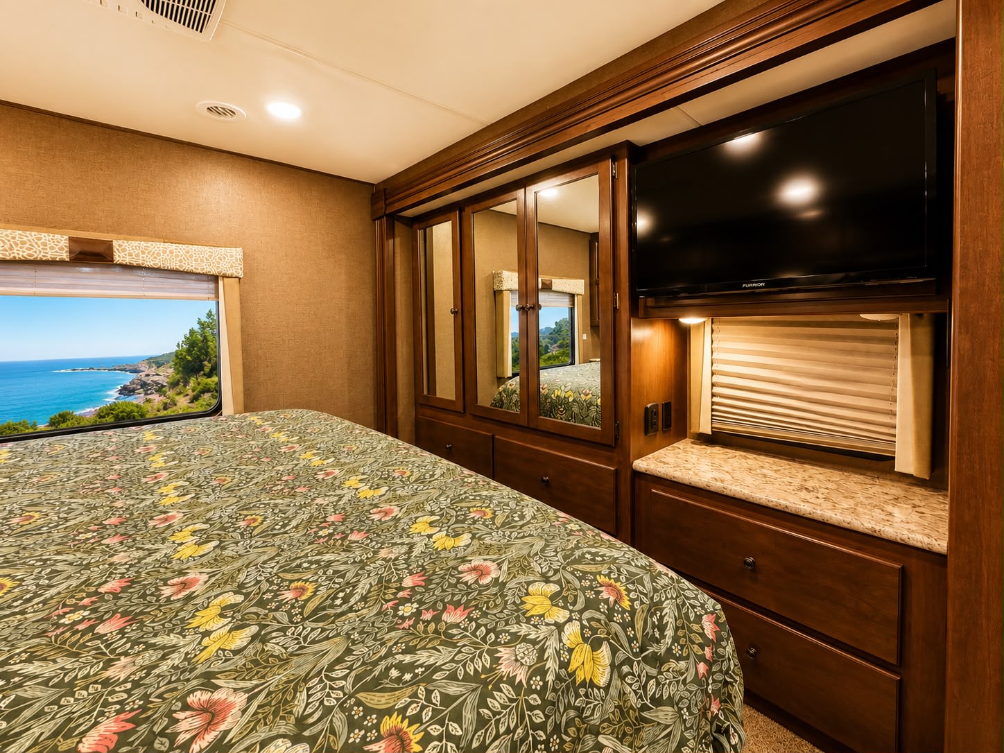 Cozy RV rental bedroom with stunning ocean view, floral bedspread, TV, and mirrored wardrobe for your next travel adventure.. Thor Windsport 2019