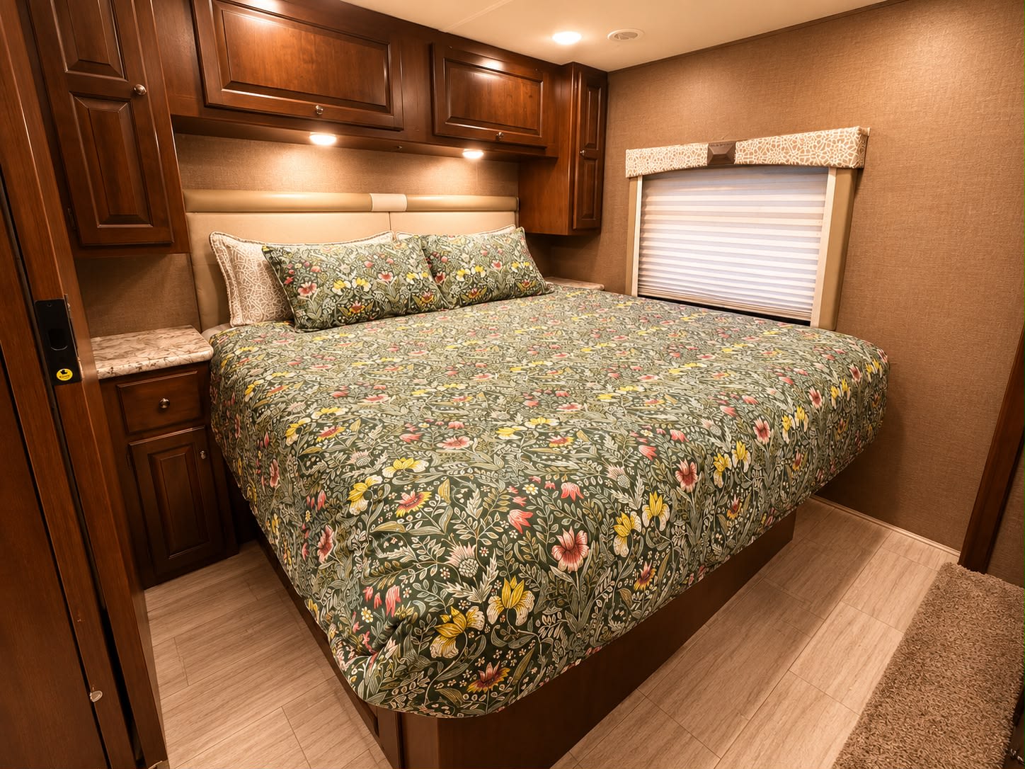 Cozy RV rental bedroom with a large bed, dark green floral comforter, wood cabinets, and a side nightstand.. Thor Windsport 2019