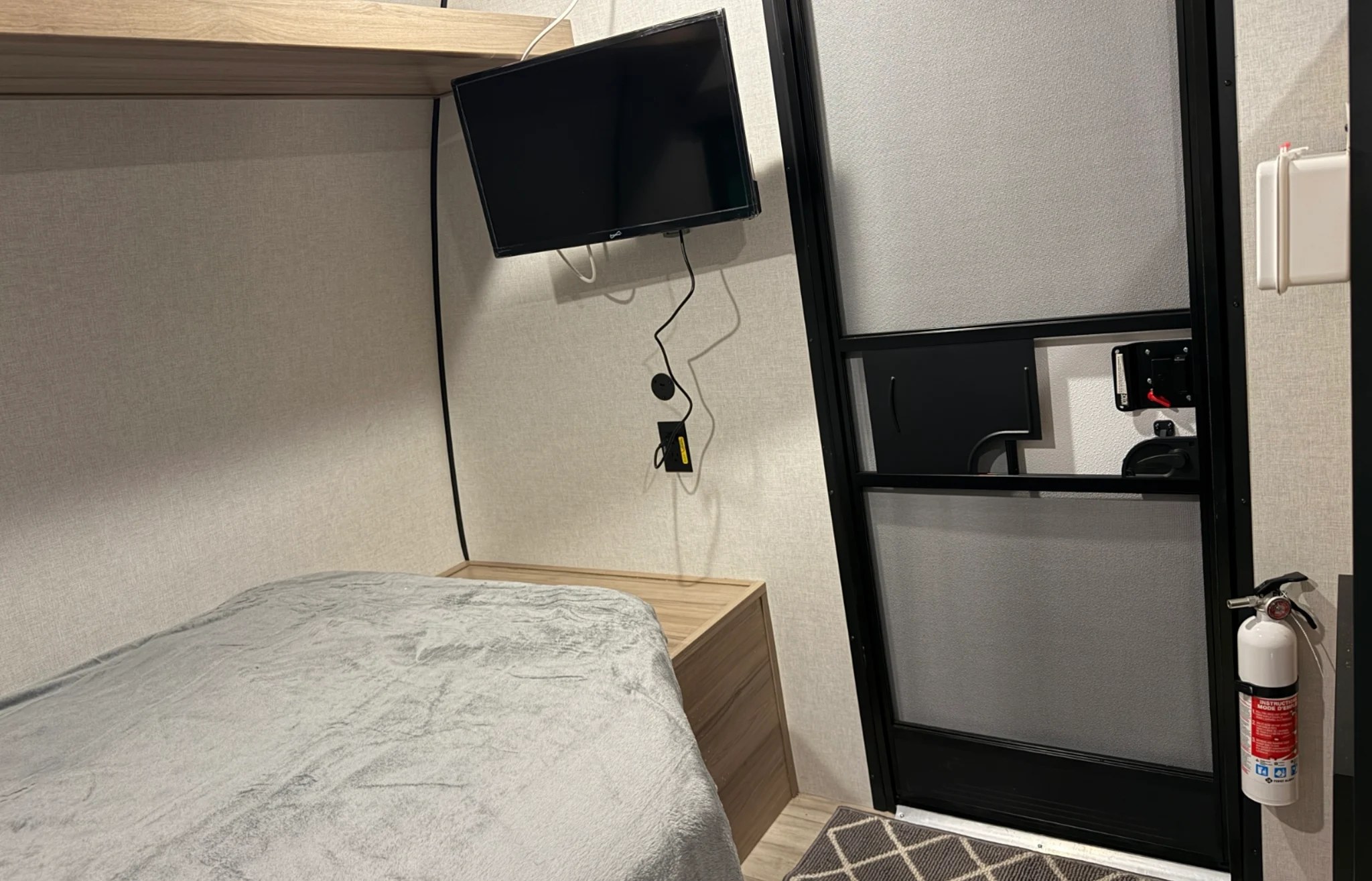 Cozy RV rental bedroom featuring a mounted TV, comfortable bed, and a fire extinguisher by the door for safety.. Keystone RV Coleman 2026