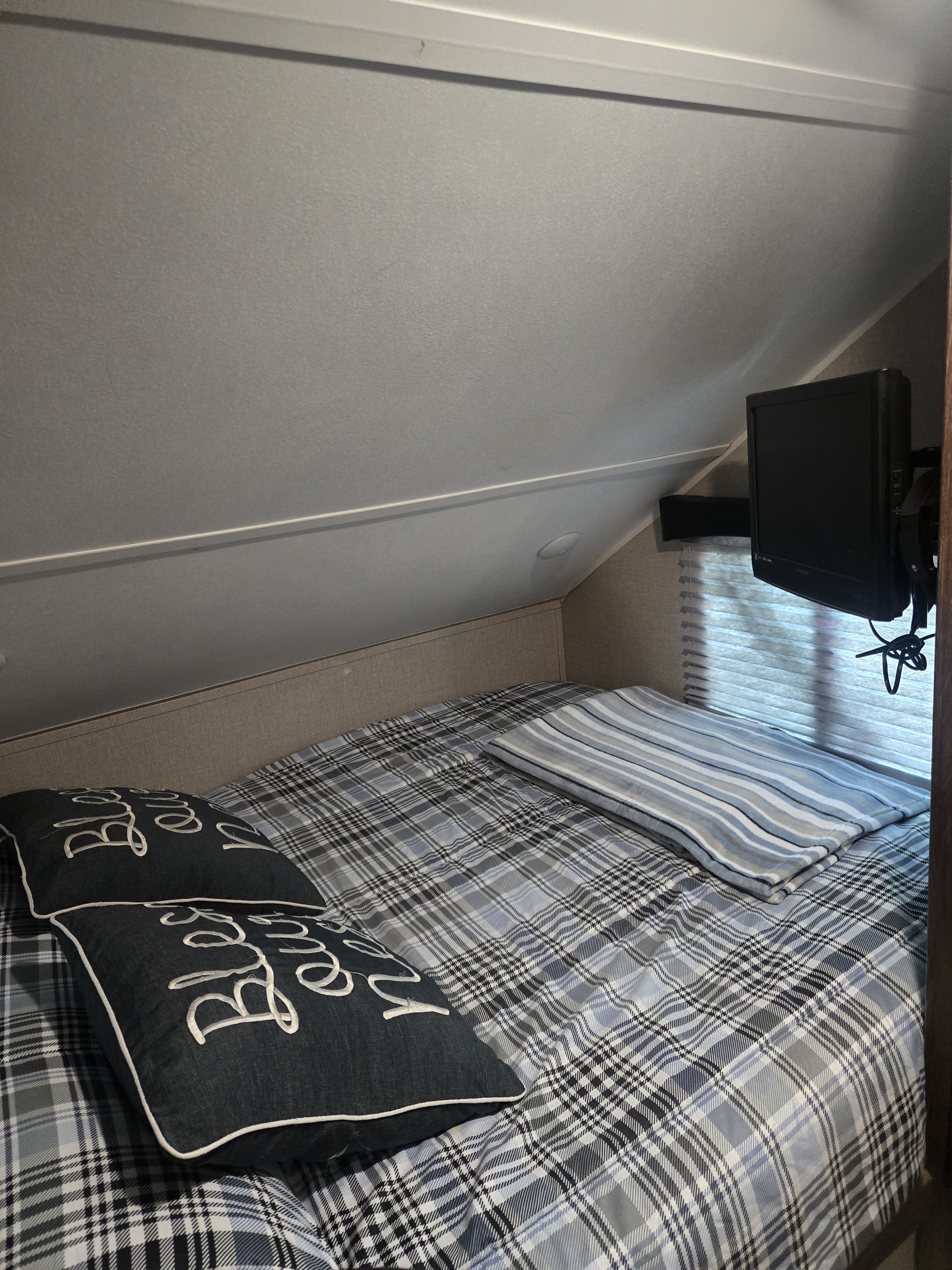 Cozy RV rental bedroom with plaid bedding, accent pillows, a folded striped blanket, and a wall-mounted TV.. Travel Lite Falcon 2019