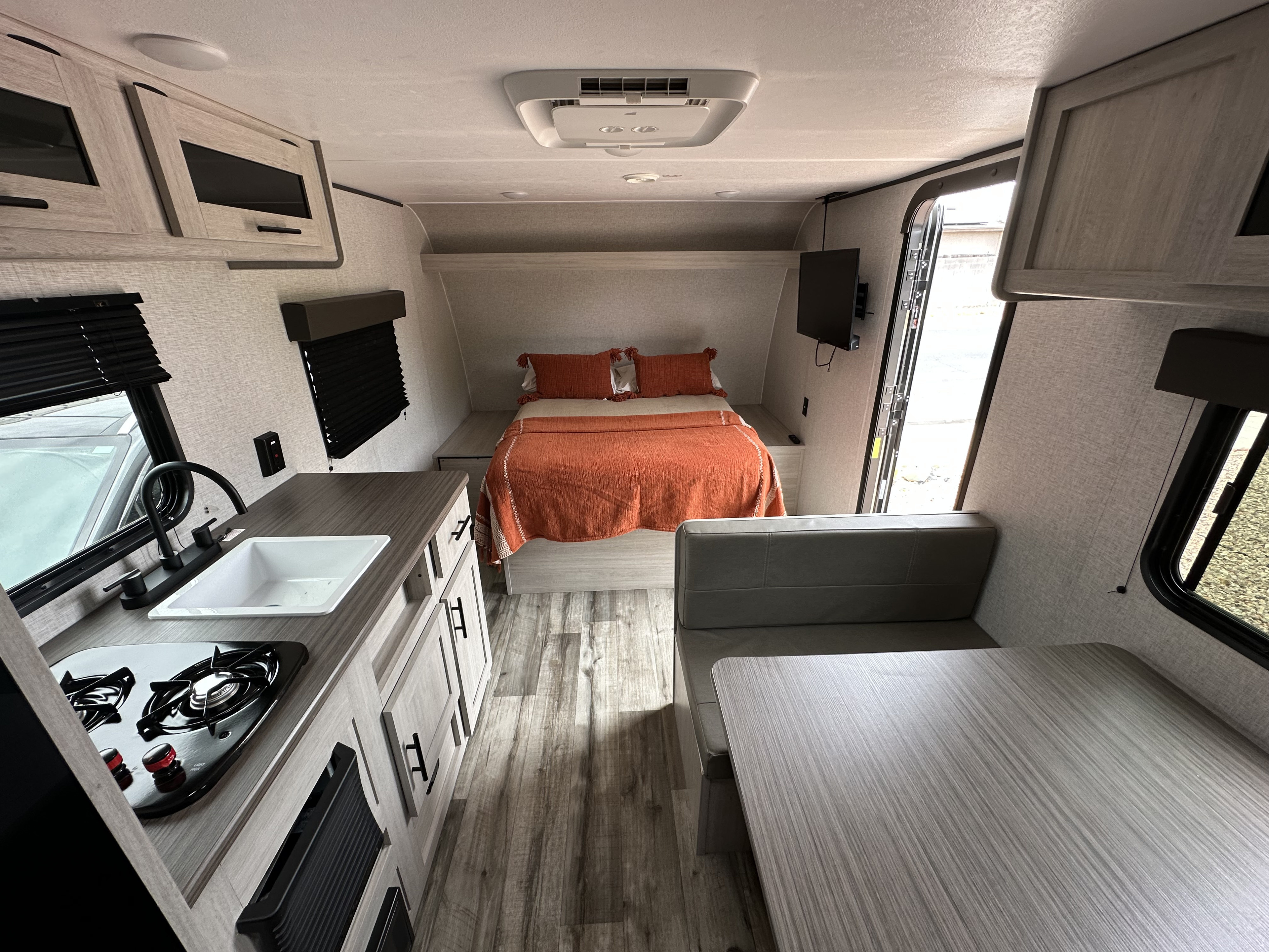 A bright, modern rv rental interior with a kitchen featuring a stove and sink, a cozy bed with orange bedding, and a dining booth.. Crossroads RV Zinger Lite 2026