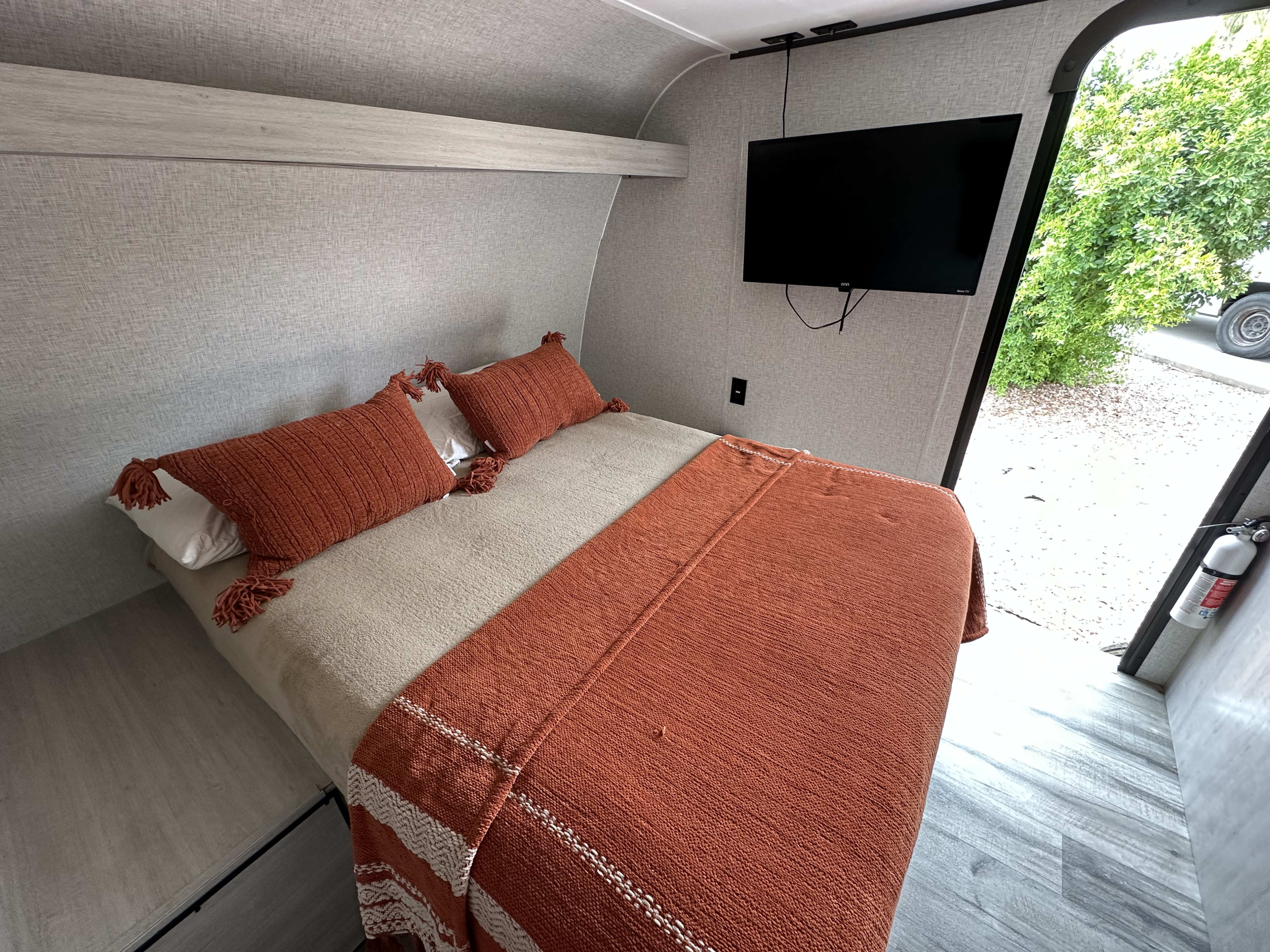 Experience comfort in this RV rental bedroom: a cozy bed with orange-tasseled pillows and a blanket, plus a wall-mounted TV.. Crossroads RV Zinger Lite 2026