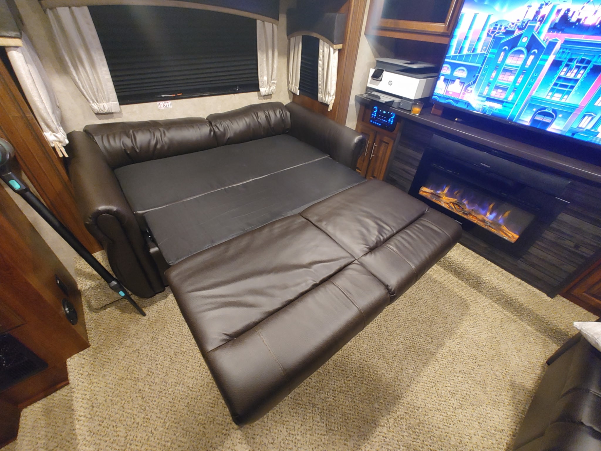 Inside an RV rental: a comfortable brown leather sofa bed extended, with a TV, electric fireplace, and window with blinds.. Jayco Eagle 2018