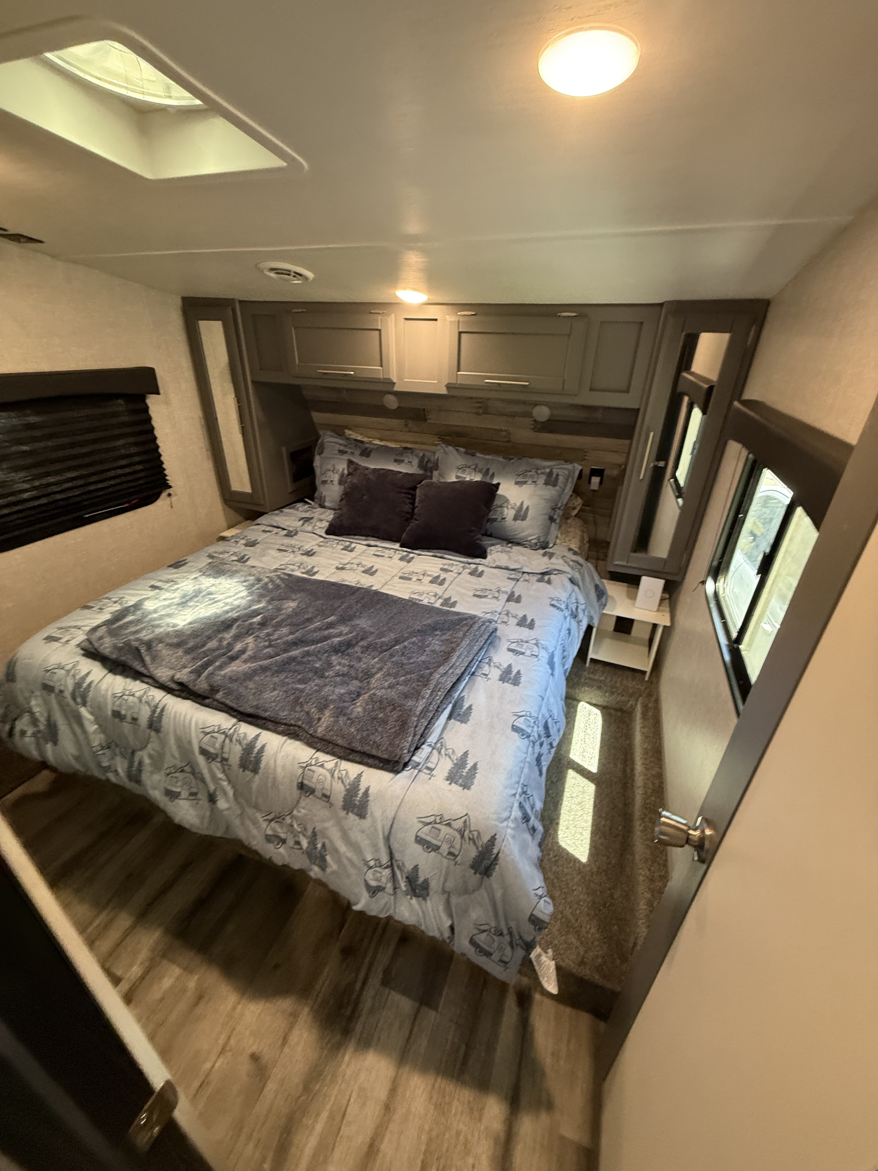 Cozy bedroom in an RV rental, featuring a bed with nature-themed bedding, overhead cabinets, windows, and a skylight.. Crossroads RV Volante 2022