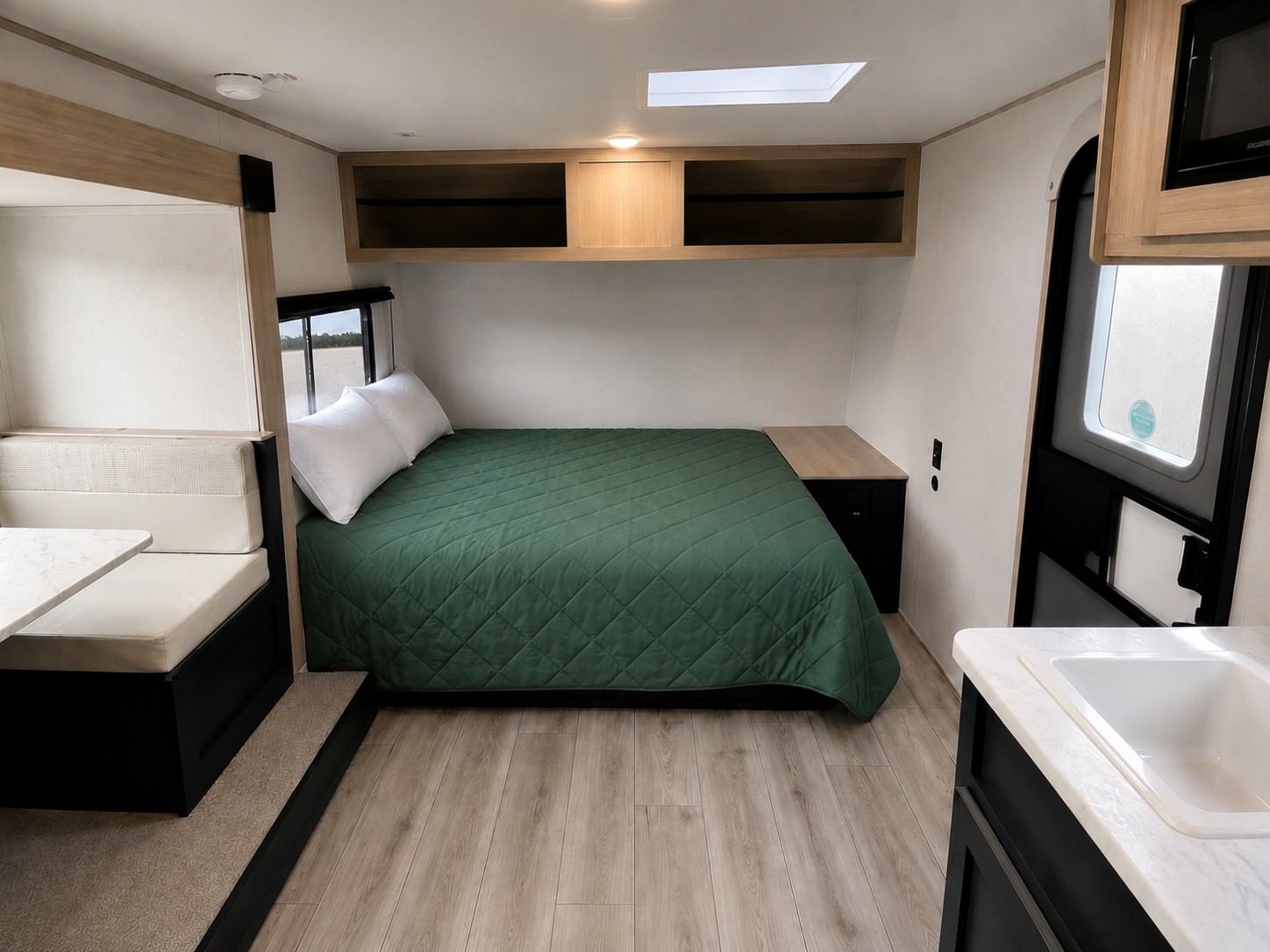 Inside an RV rental: a neat bedroom with green bedding, dinette, and compact kitchen area. Bright and clean travel trailer.. Forest River Avenger 2025
