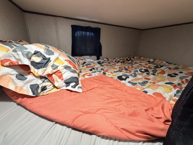 Cozy RV rental sleeping area with a colorful patterned comforter and coral blanket, offering a snug bunk for your trip.. Jayco Jay Flight SLX 2021