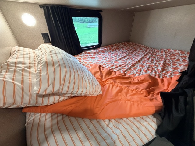 Rv rental camper bed: cozy sleeping area with orange and white striped pillows, patterned sheets, and a window view.. Jayco Jay Flight SLX 2021