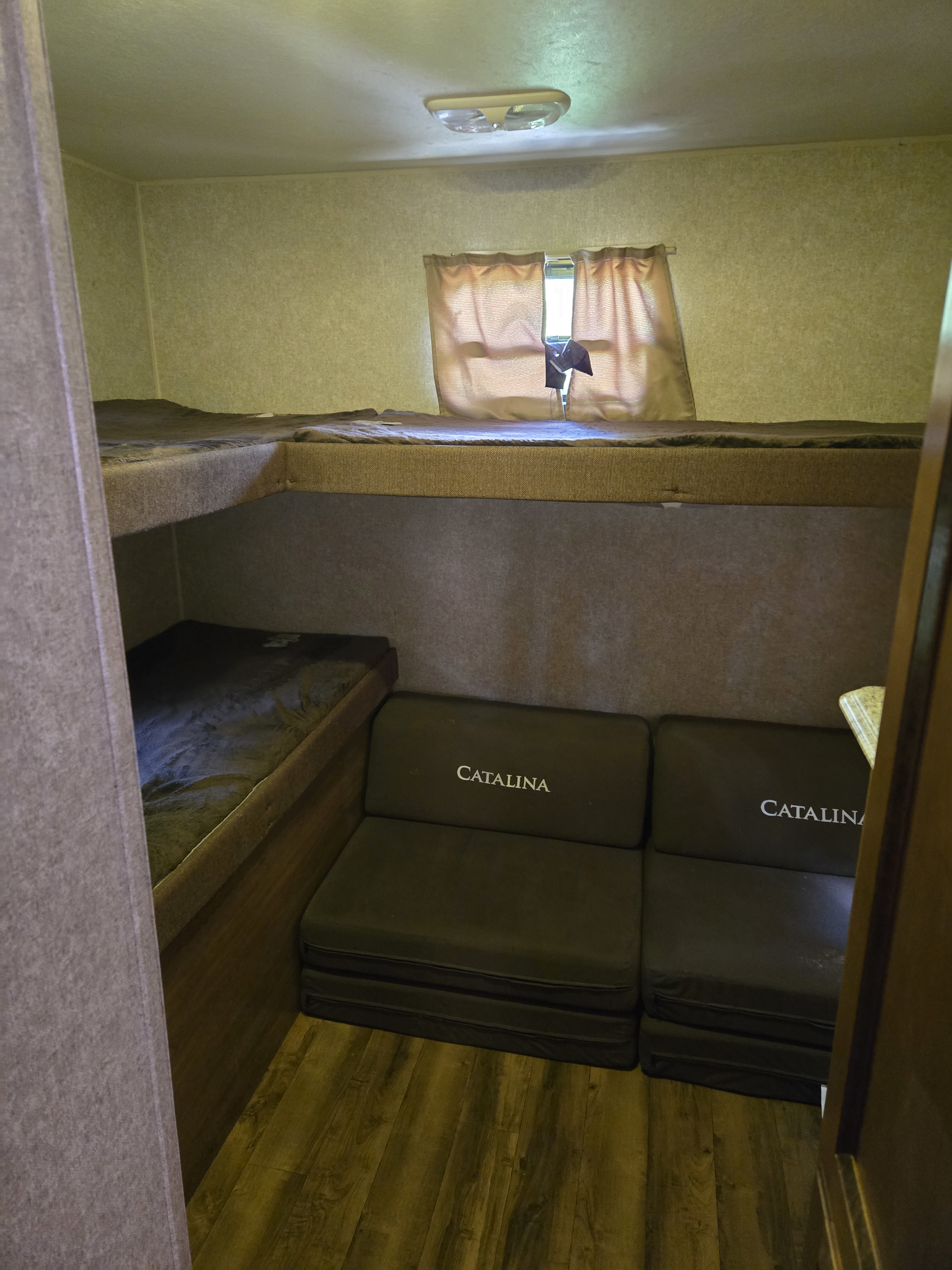 Cozy RV rental interior with bunk beds, a window with curtains, and "CATALINA" branded folding seating for travelers.. Coachmen Catalina 2017