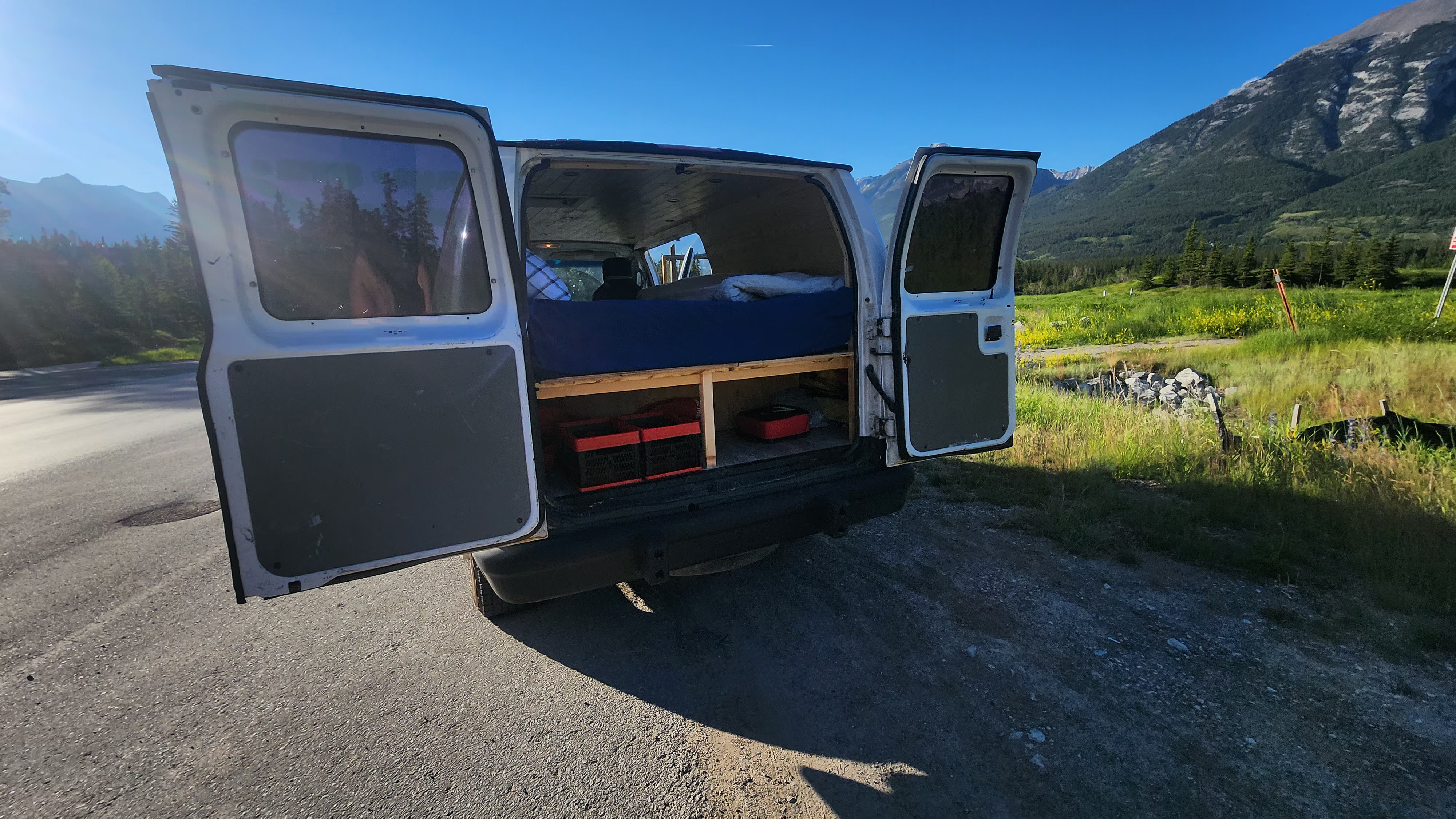 RV rental campervan with open doors reveals a cozy bed & storage, ready for mountain road trips.. Ford Econoline 2011