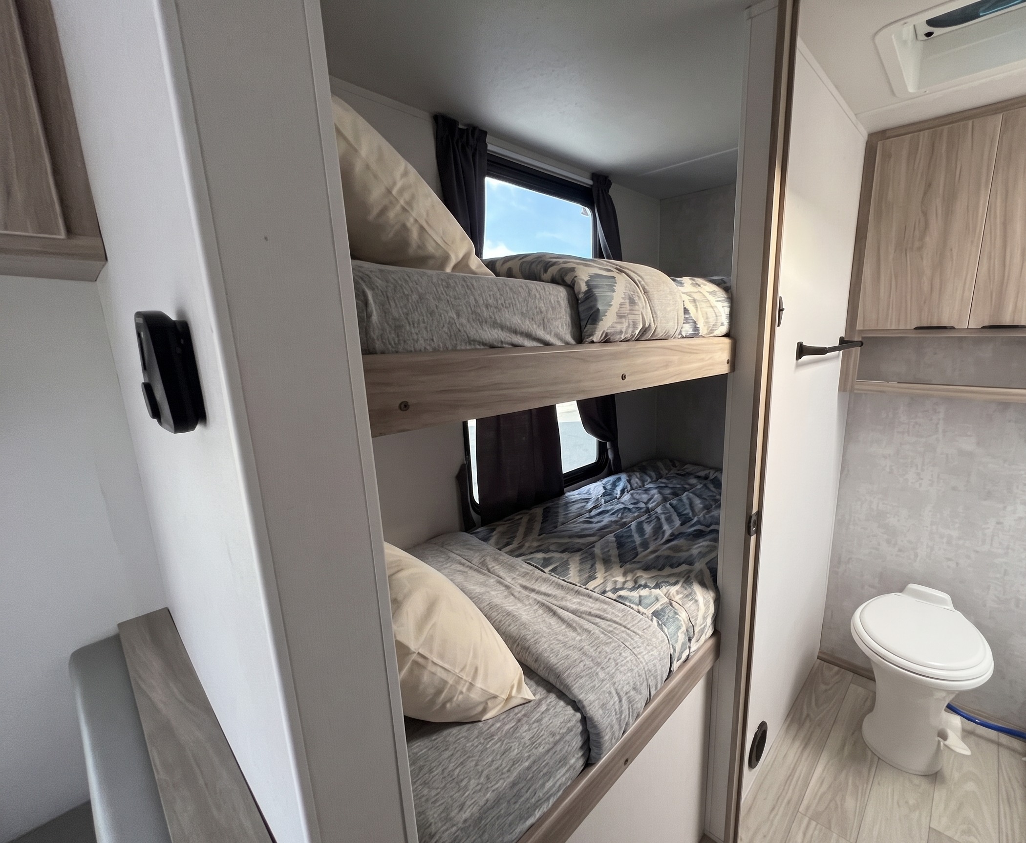 Two bunk beds with patterned bedding are seen next to a compact toilet area in this cozy **rv rental**.. Winnebago Access 2025