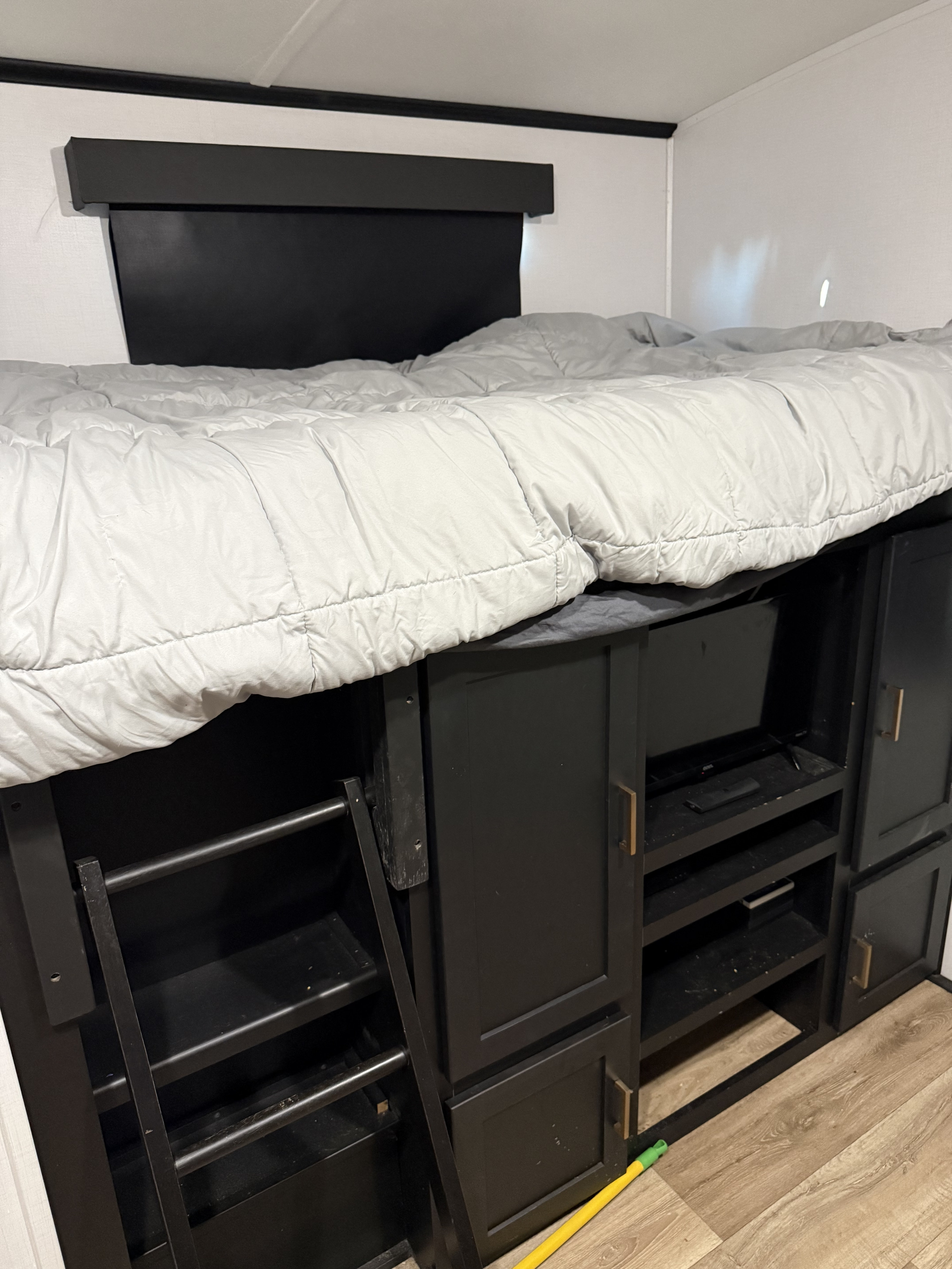 RV rental bunk bed with integrated storage, TV, and ladder below. Features gray bedding and black cabinet-style furniture.. Keystone RV Outback 2023