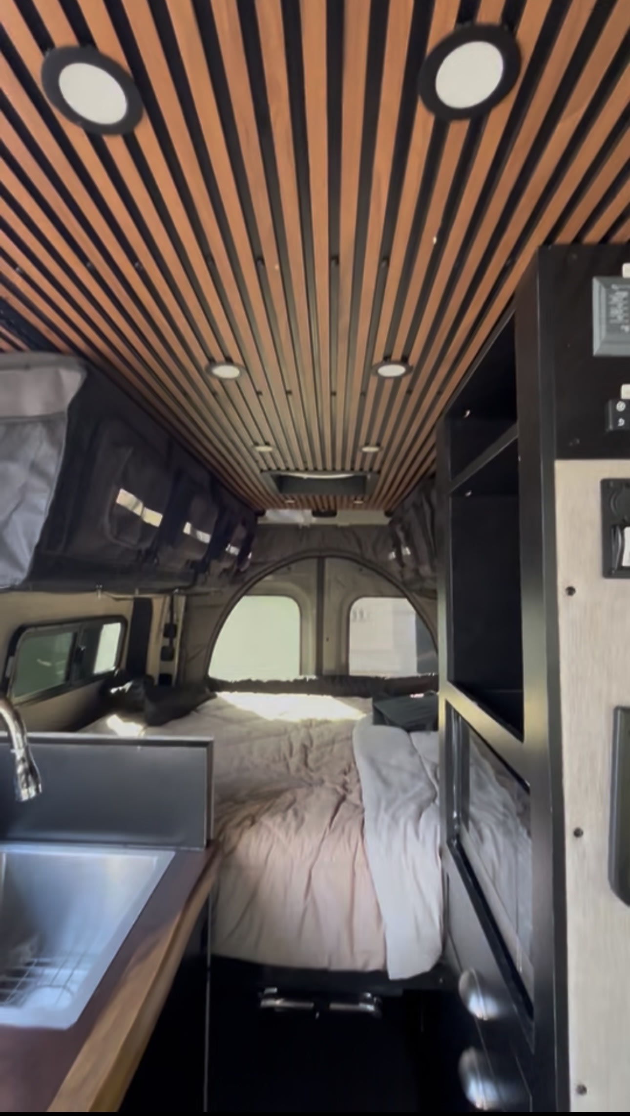 RV rental interior: wood-slatted ceiling, bed, kitchen sink, & storage. Modern camper van ready for your journey.. Mercedes Sprinter 2022