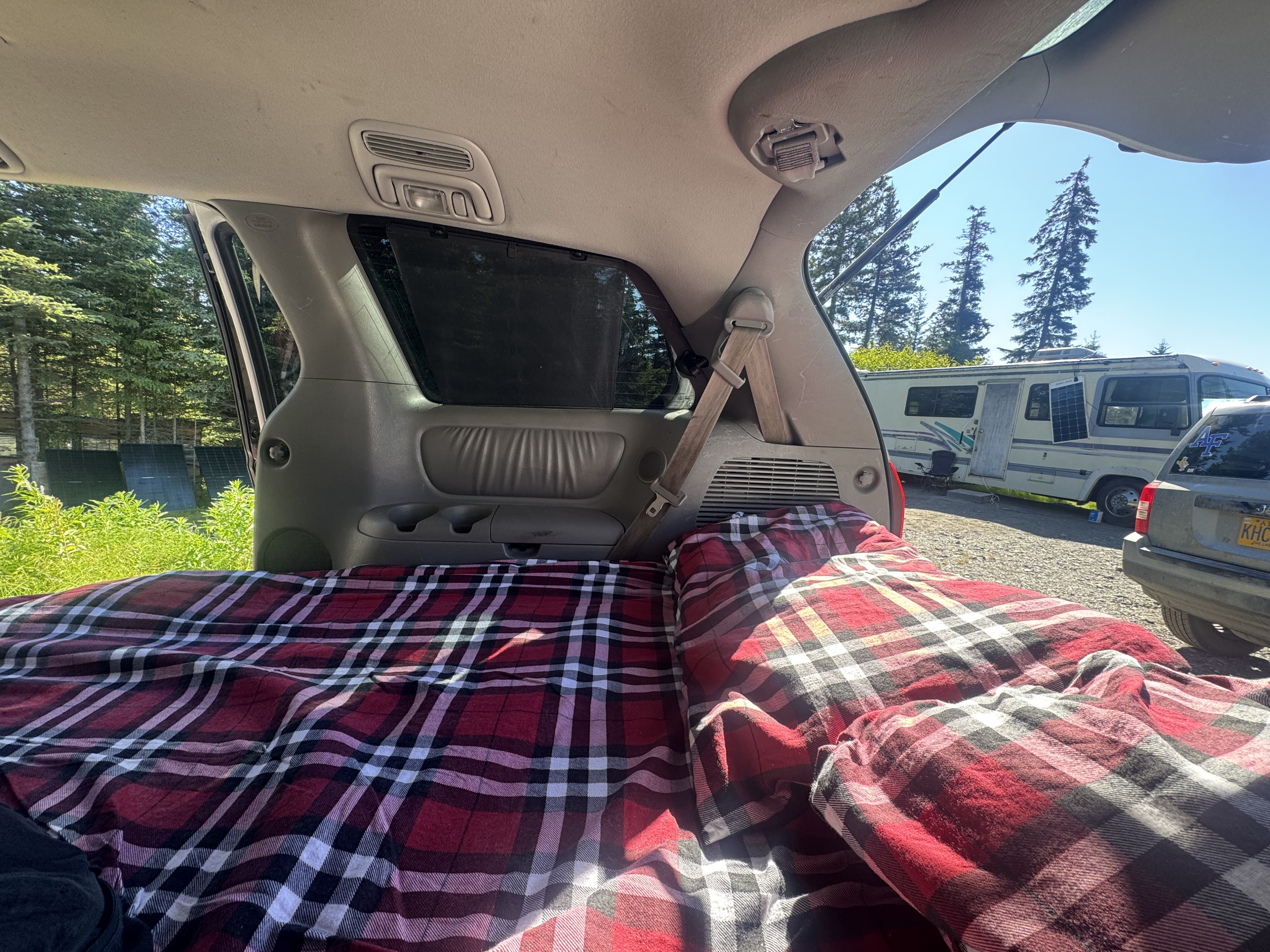 Cozy car camping bed (plaid) in SUV. View of an RV rental, trees, and sky from the open hatch. Perfect for a road trip!. Toyota Toyota Sienna XLE 2005