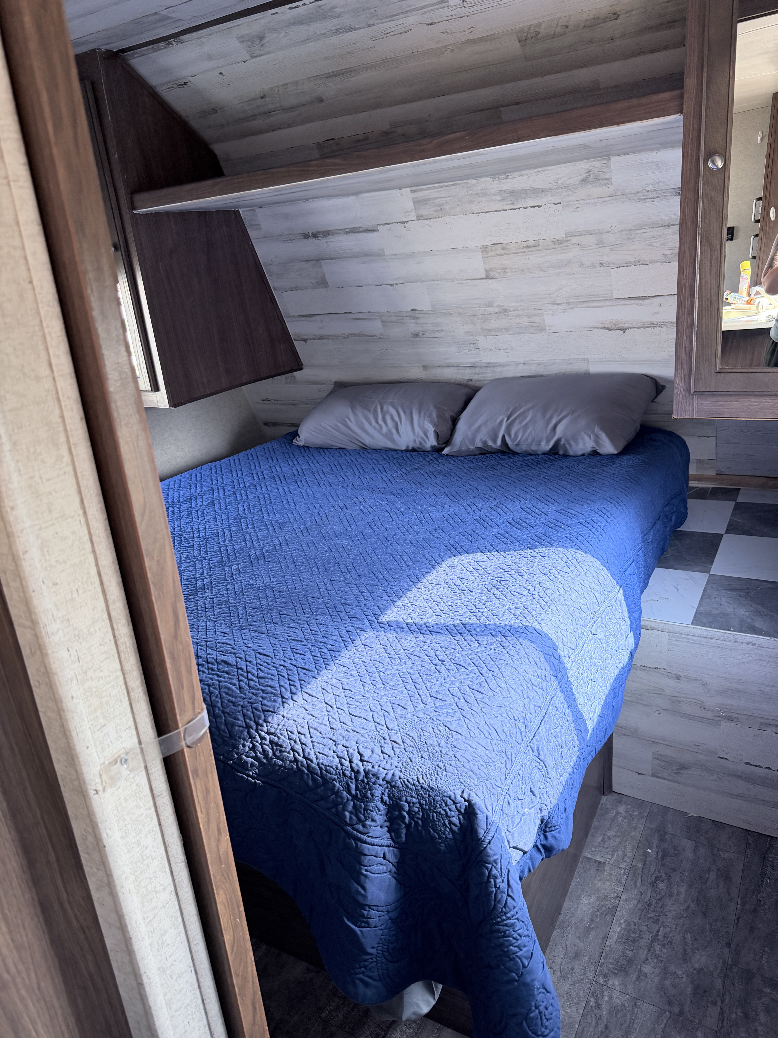 Cozy RV rental bedroom with a blue quilted bed, grey pillows, and light wood-look walls, perfect for travelers.. Heartland RVs Trail Runner SLE 2018