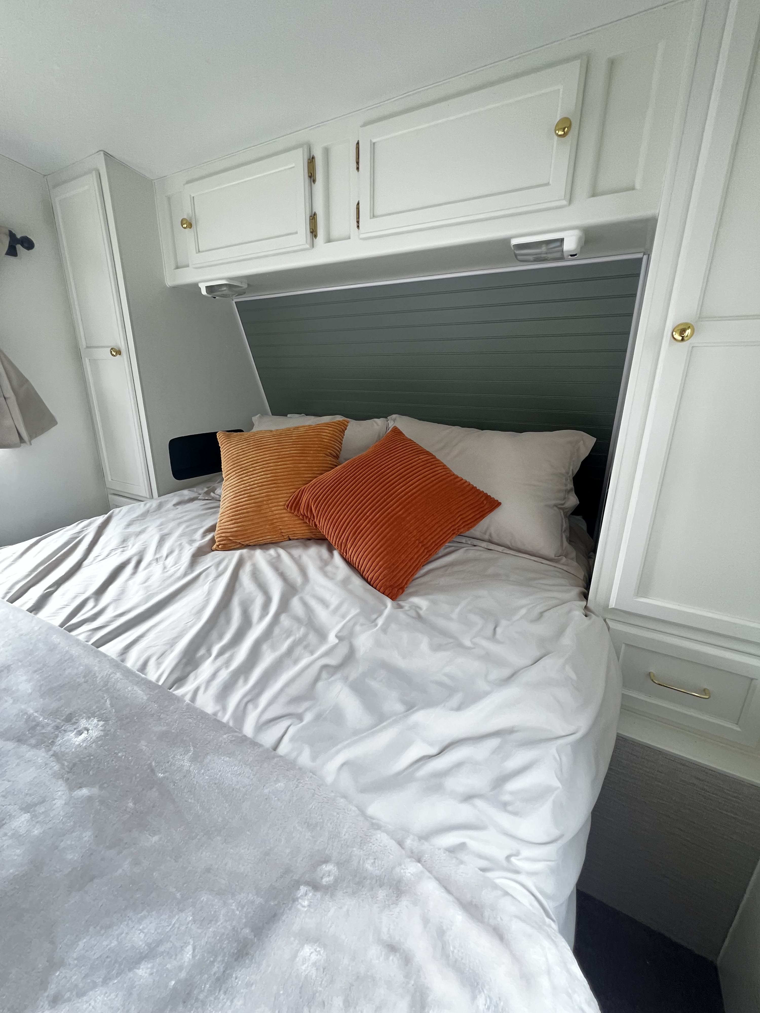Cozy RV rental bedroom interior with gray bedding, vibrant orange pillows, and ample white built-in storage cabinets.. Kustom Koach Westwind 2004
