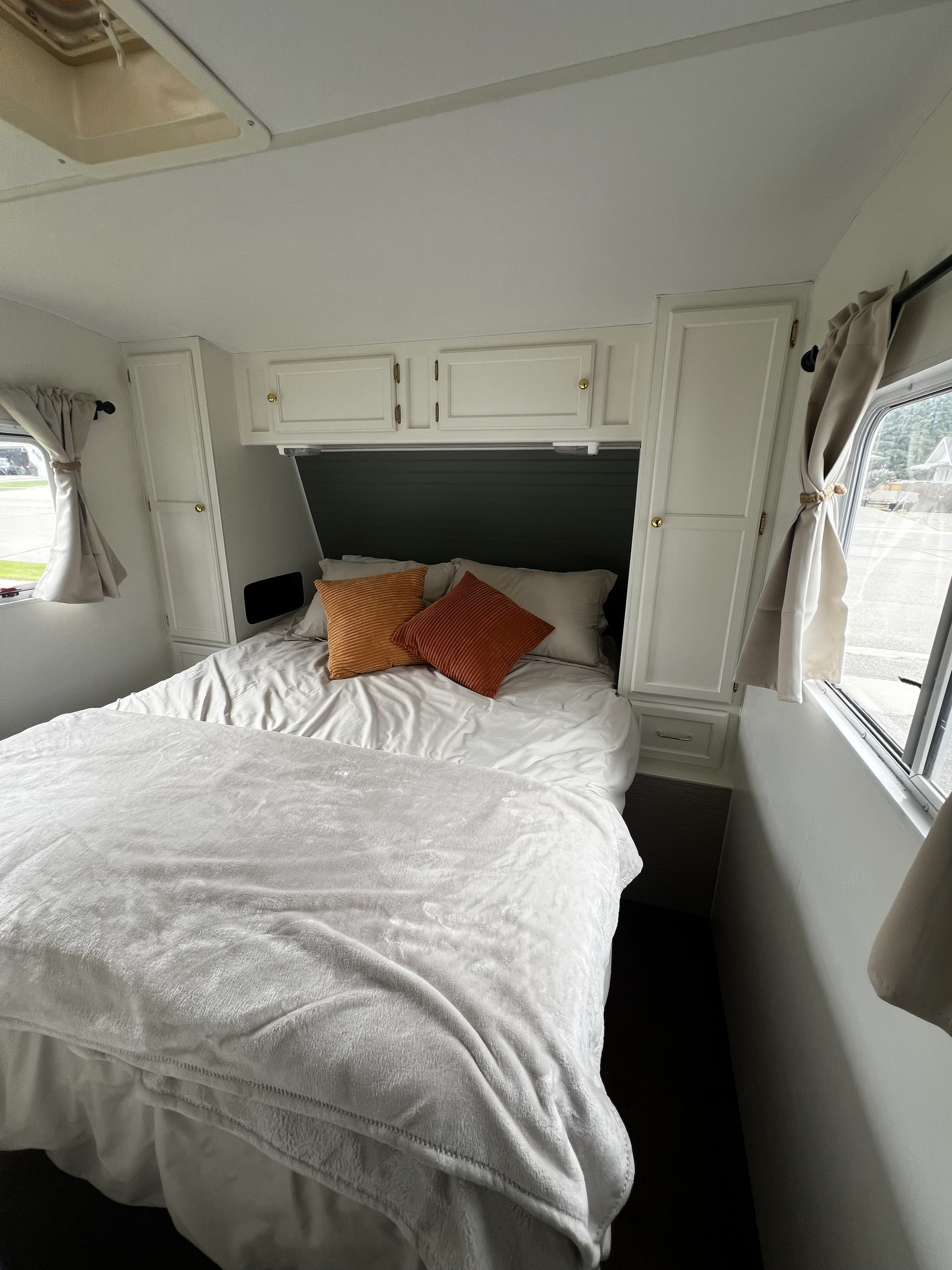 Bright RV rental bedroom interior with a neatly made bed, orange pillows, white cabinets, and windows.. Kustom Koach Westwind 2004