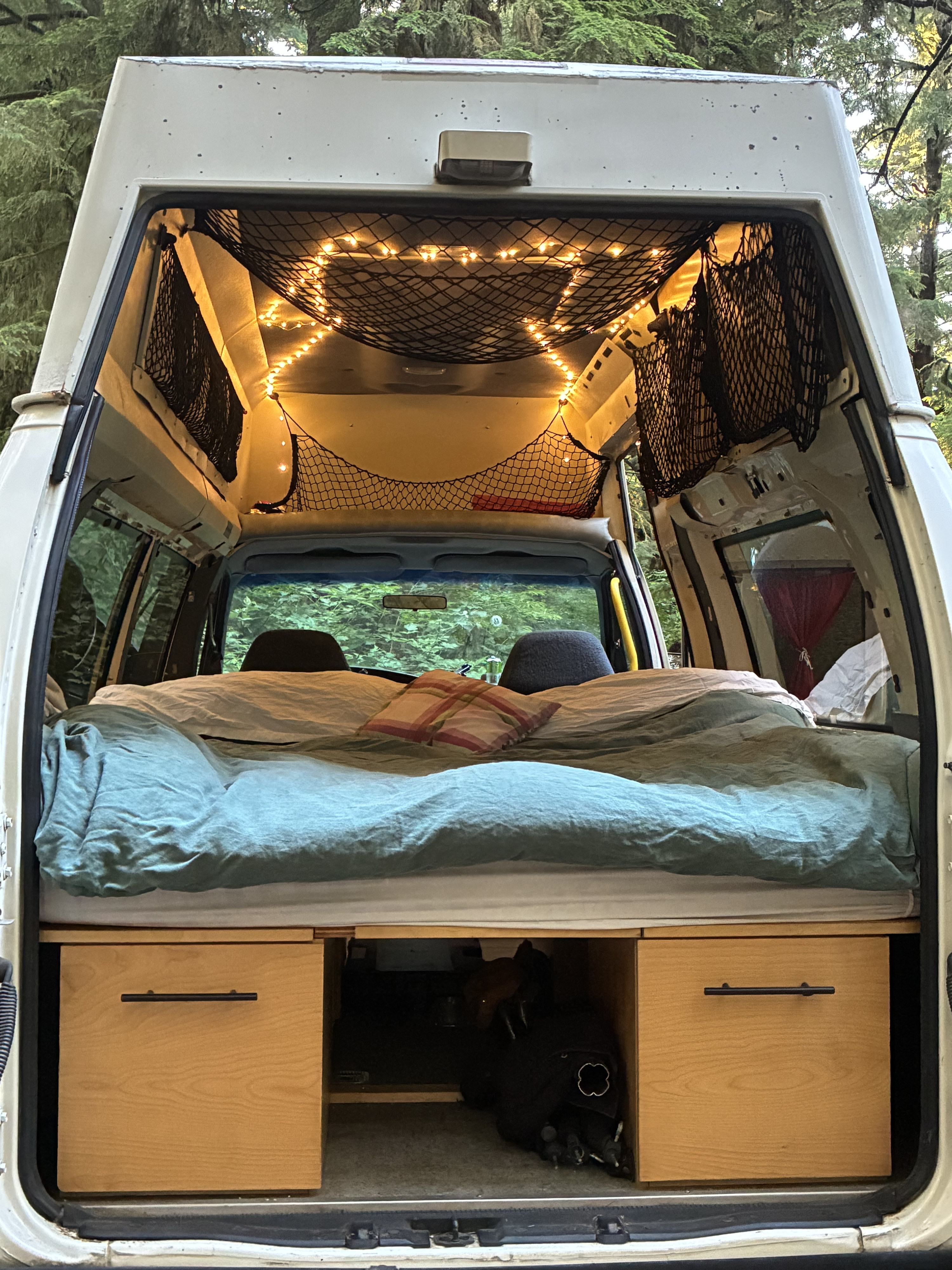 Cozy RV rental interior featuring a comfy bed, string lights, storage nets, and wooden drawers, perfect for adventures.. Ford Econoline E250supercab 1996