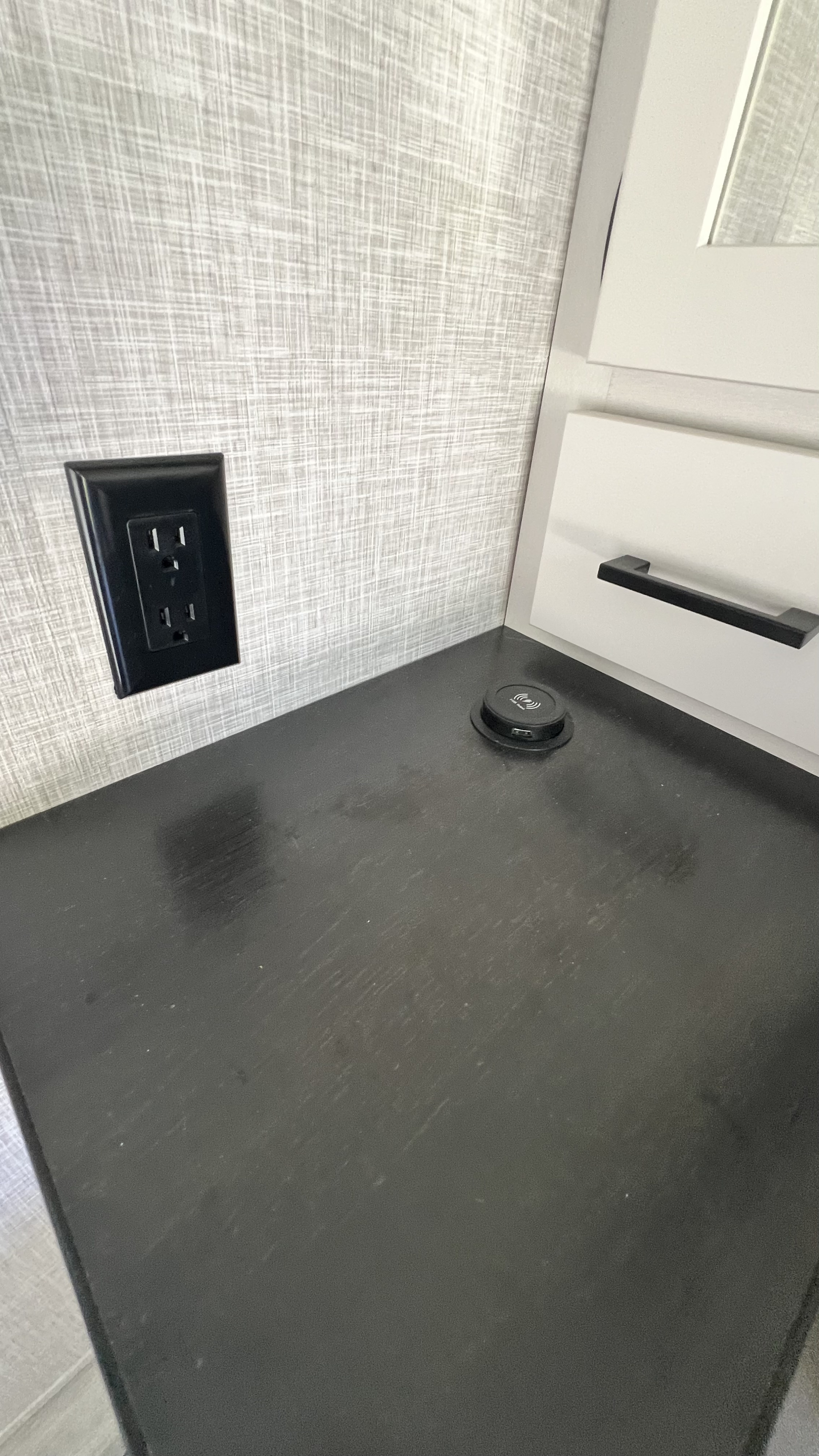 RV rental interior with a wall outlet, wireless charging pad on a dark counter, and a white storage drawer.. Highland Ridge RV Open Range 2024