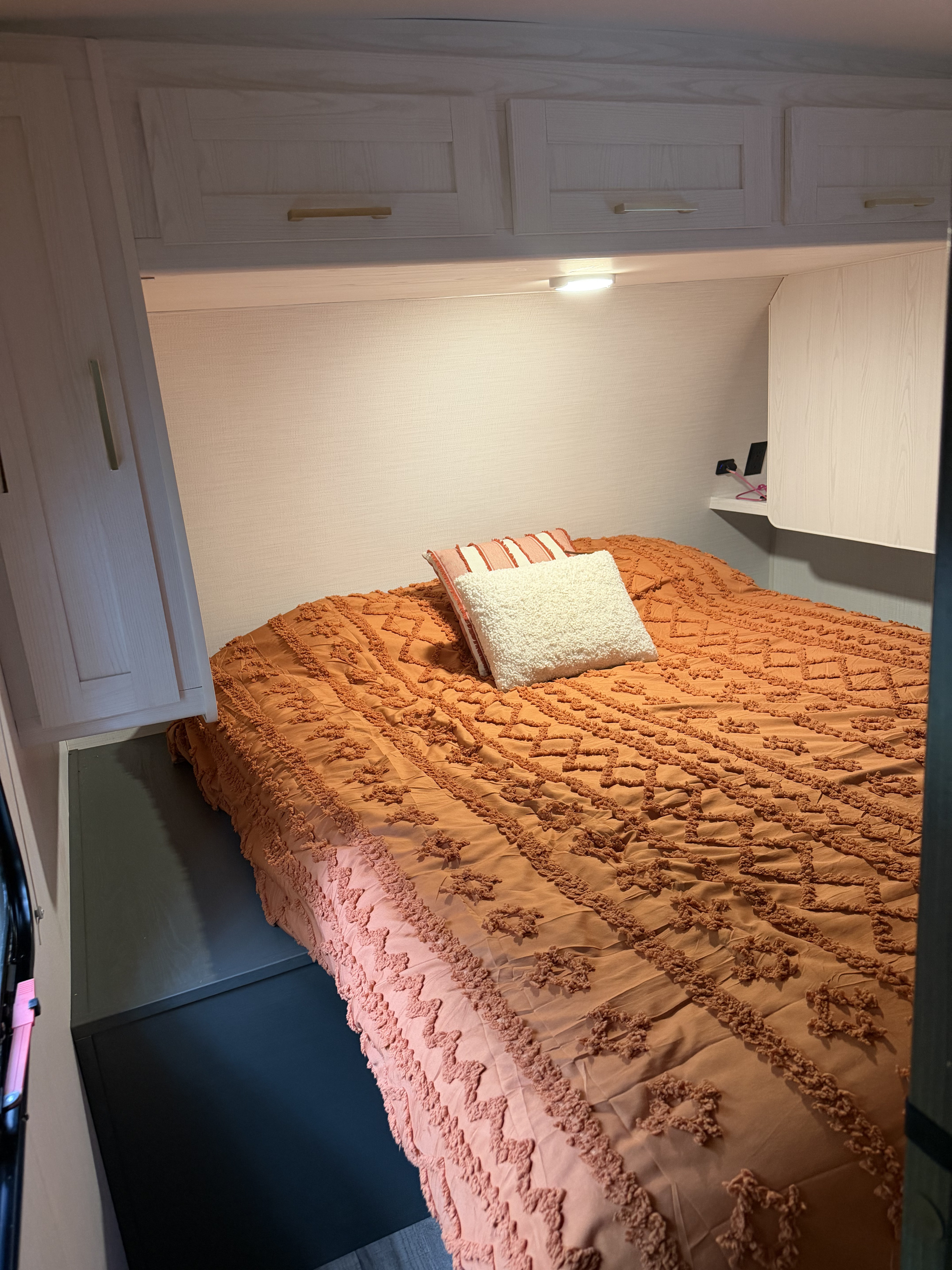 RV rental bedroom interior: comfy orange textured bed, soft pillows, bright overhead cabinets, and under-cabinet lighting.. Heartland RVs Eddie Bauer 2024