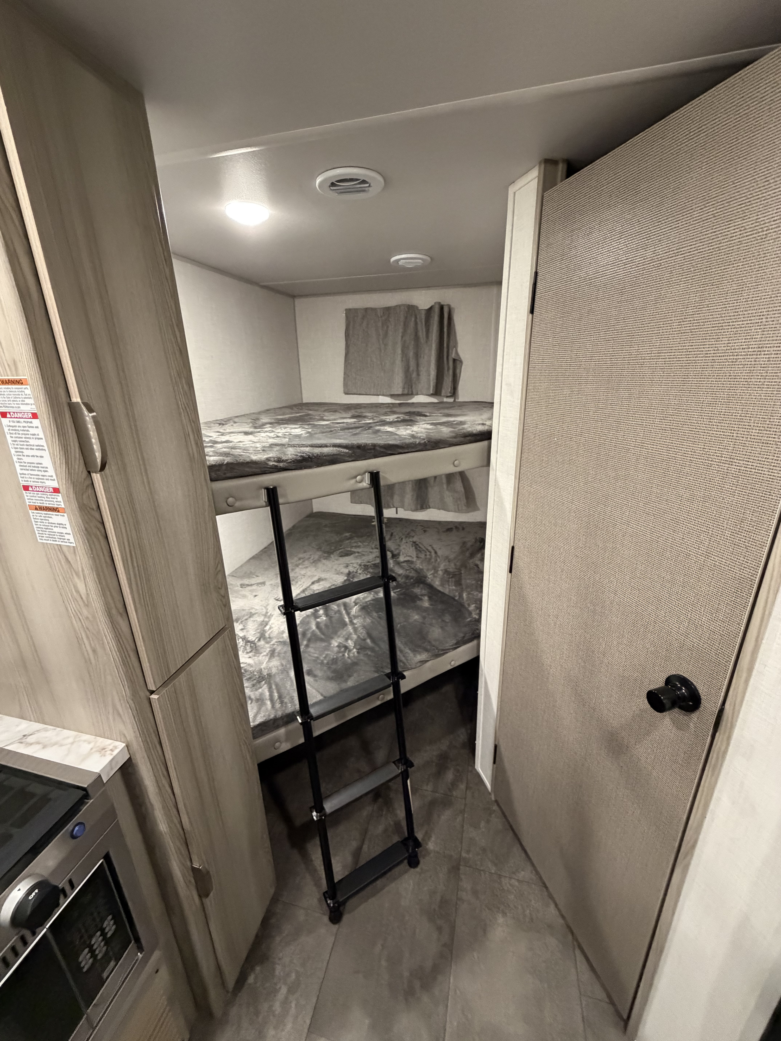 RV rental interior: two bunk beds with a ladder, a compact kitchen counter, and a door for a cozy stay.. Forest River Wildwood FSX 2024
