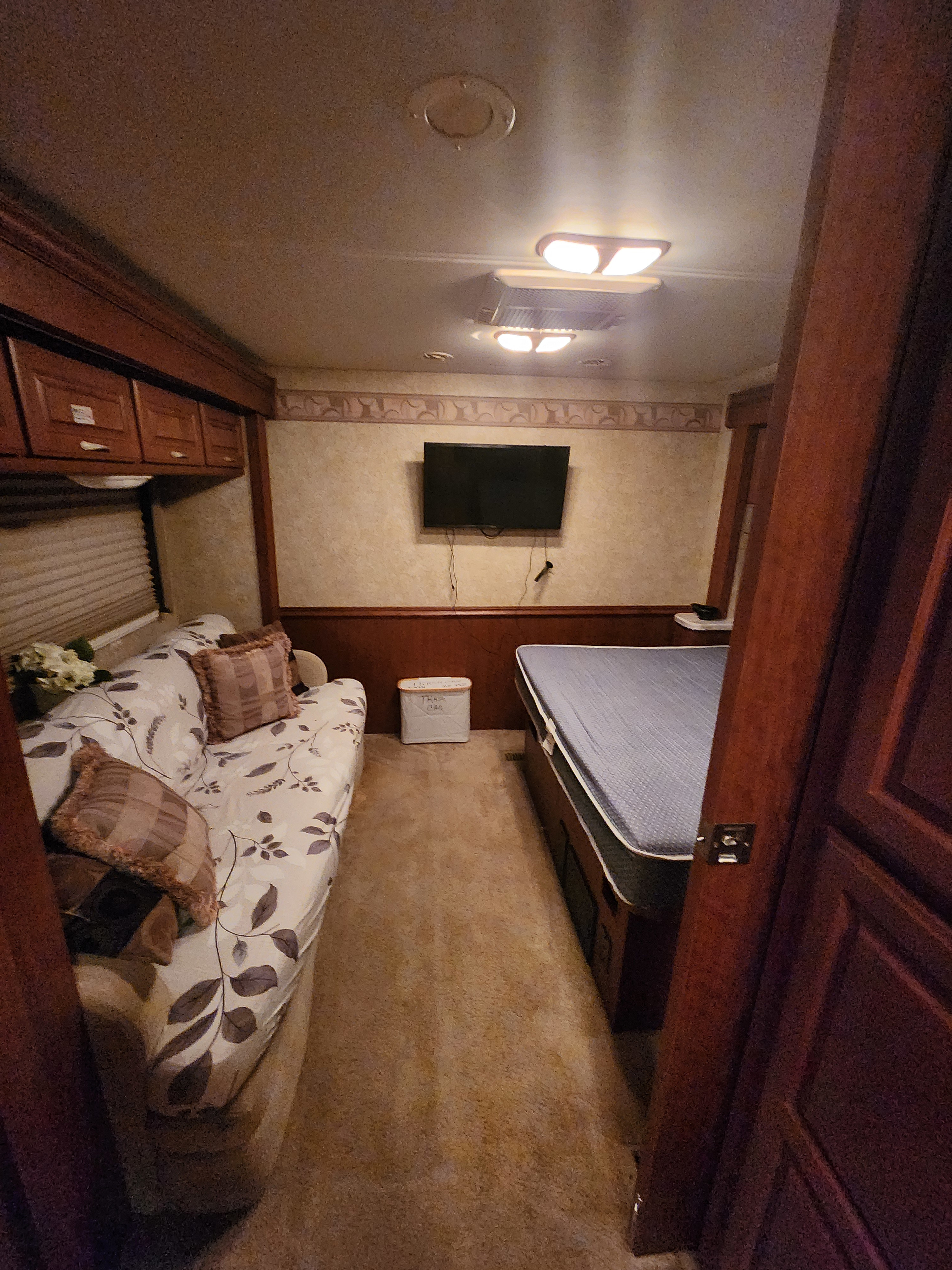 Cozy RV rental interior with a floral sofa, mounted TV, and a comfortable bed, offering a compact living space.. Four Winds Hurricane 2007