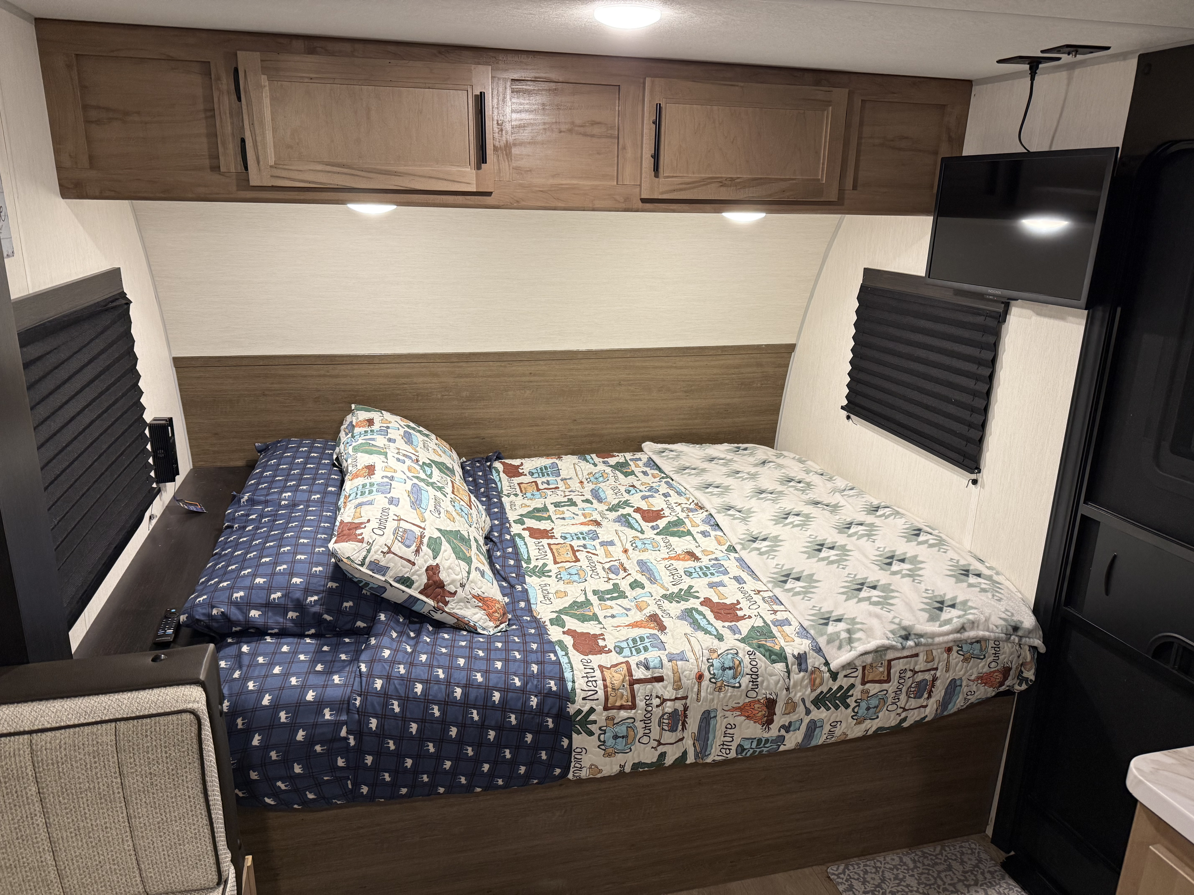 Cozy RV rental bedroom with nature-themed bedding, overhead cabinets, and a TV for relaxing after camping adventures.. Forest River Cherokee Wolf Pup 2025