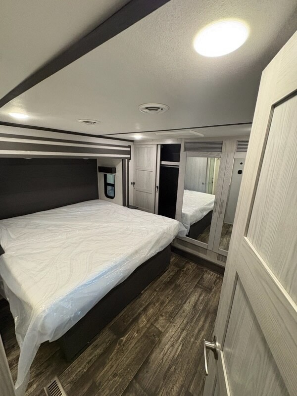Modern RV rental bedroom with a queen bed (plastic wrapped), wood-look floor, and mirrored closet. Ideal for your journey.. Keystone Fuzion 2021