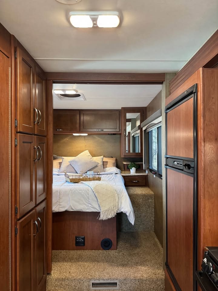 Step inside this inviting RV rental bedroom featuring a plush bed, warm wood cabinetry, and soft carpet, ready for your road trip comfort.. A.C.E. A.C.E. Motorhome 2015