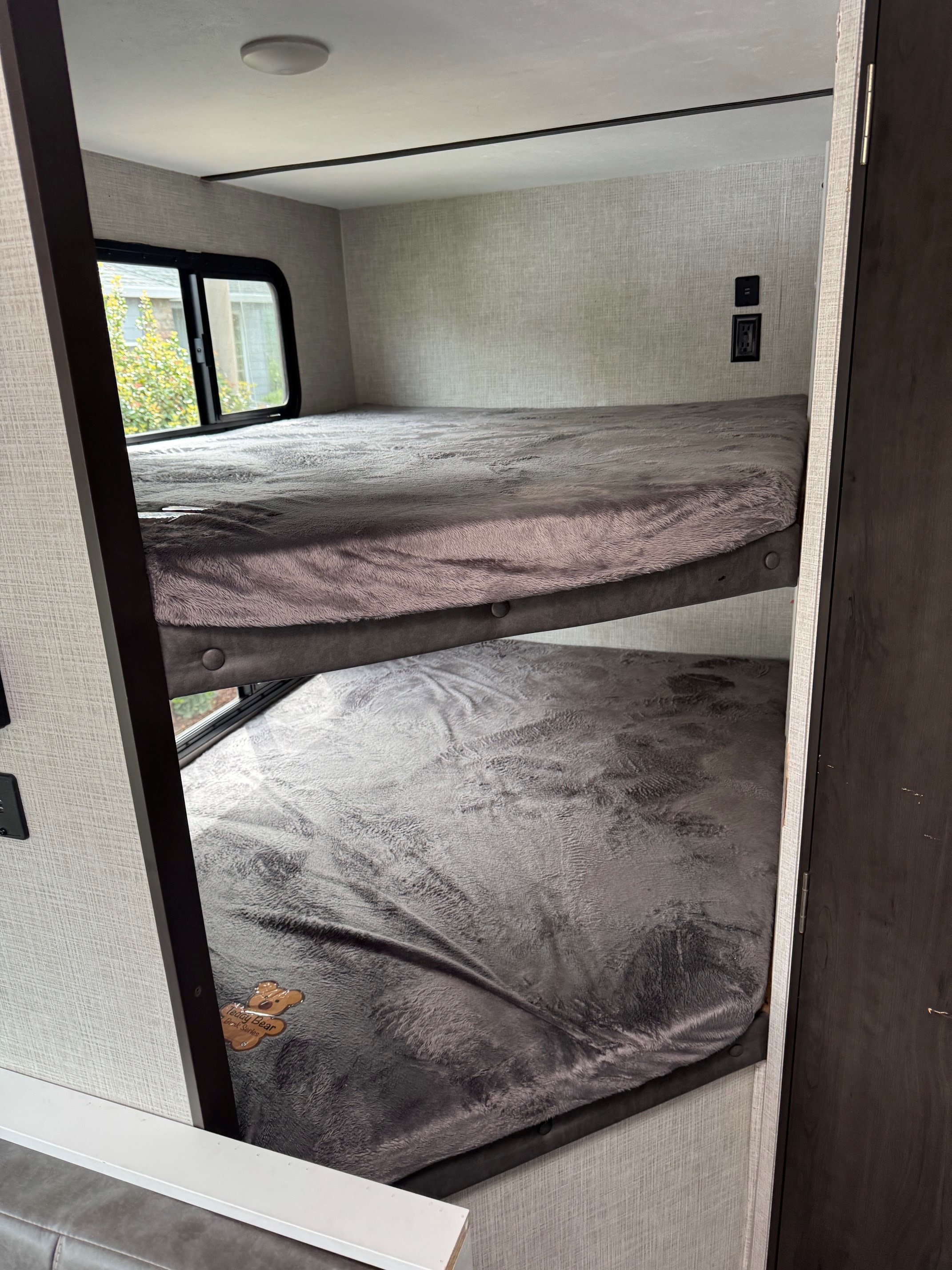 RV rental features two comfy bunk beds with soft gray blankets, a window, and wall outlets, great for family travel.. Keystone RV Bullet Crossfire 2020
