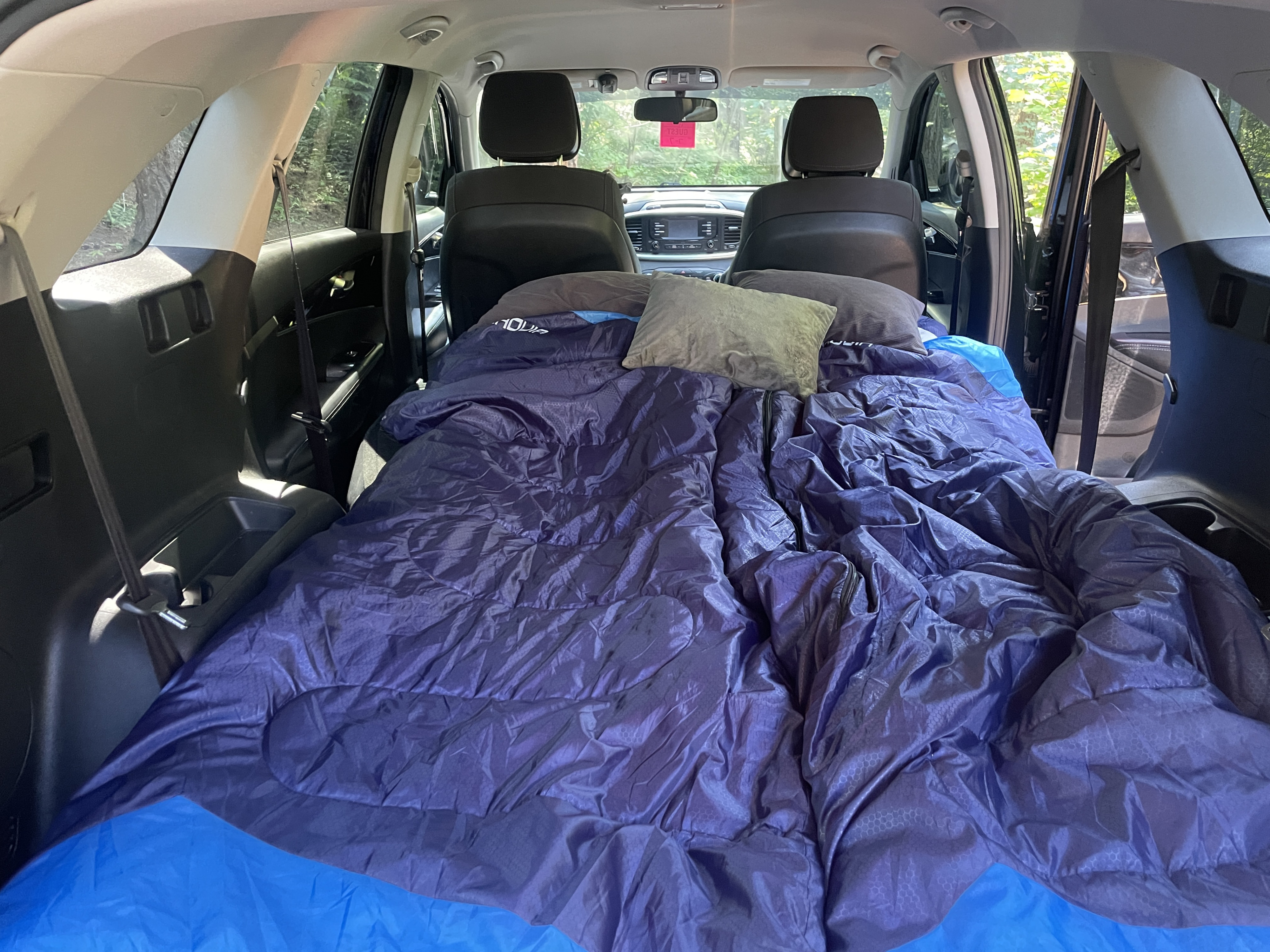 Inside an SUV, a blue sleeping bag & pillows make a comfy car camping setup, a versatile alternative to an rv rental for travel.. KIA Sorento 4X4 2017